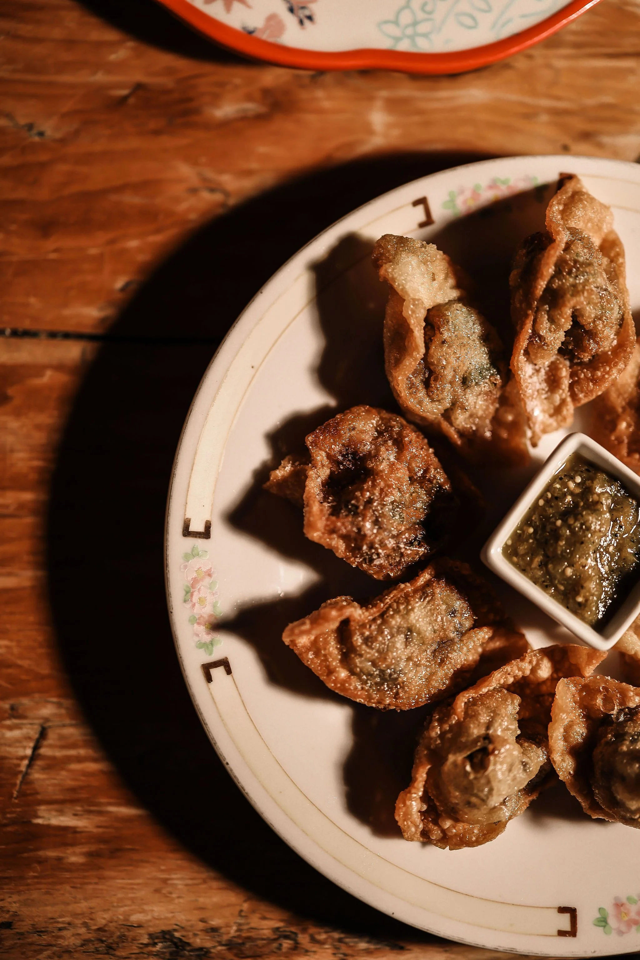 Fried dumplings served with dipping sauce on a white floral plate.