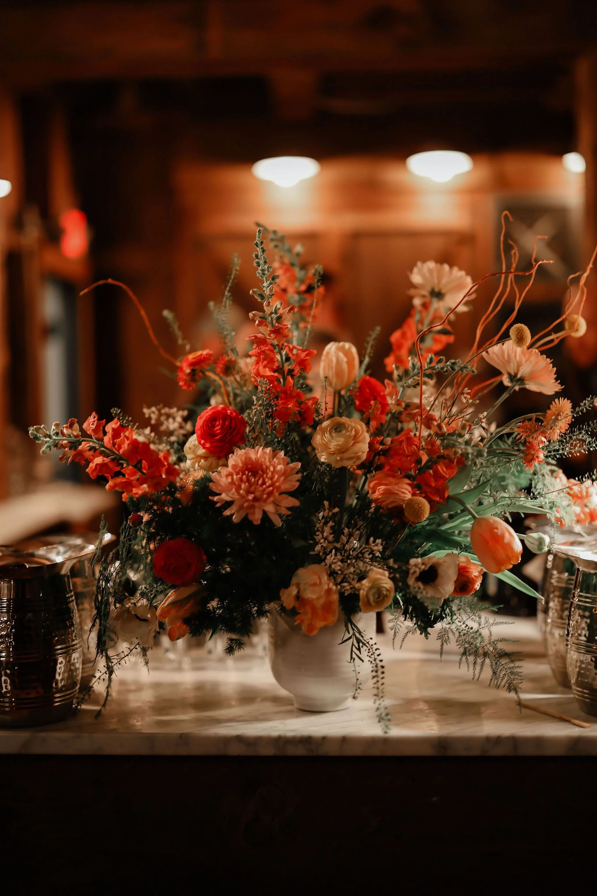 A large, colorful flower arrangement in a white vase on a marble table, with a wooden-paneled background and dim lighting.