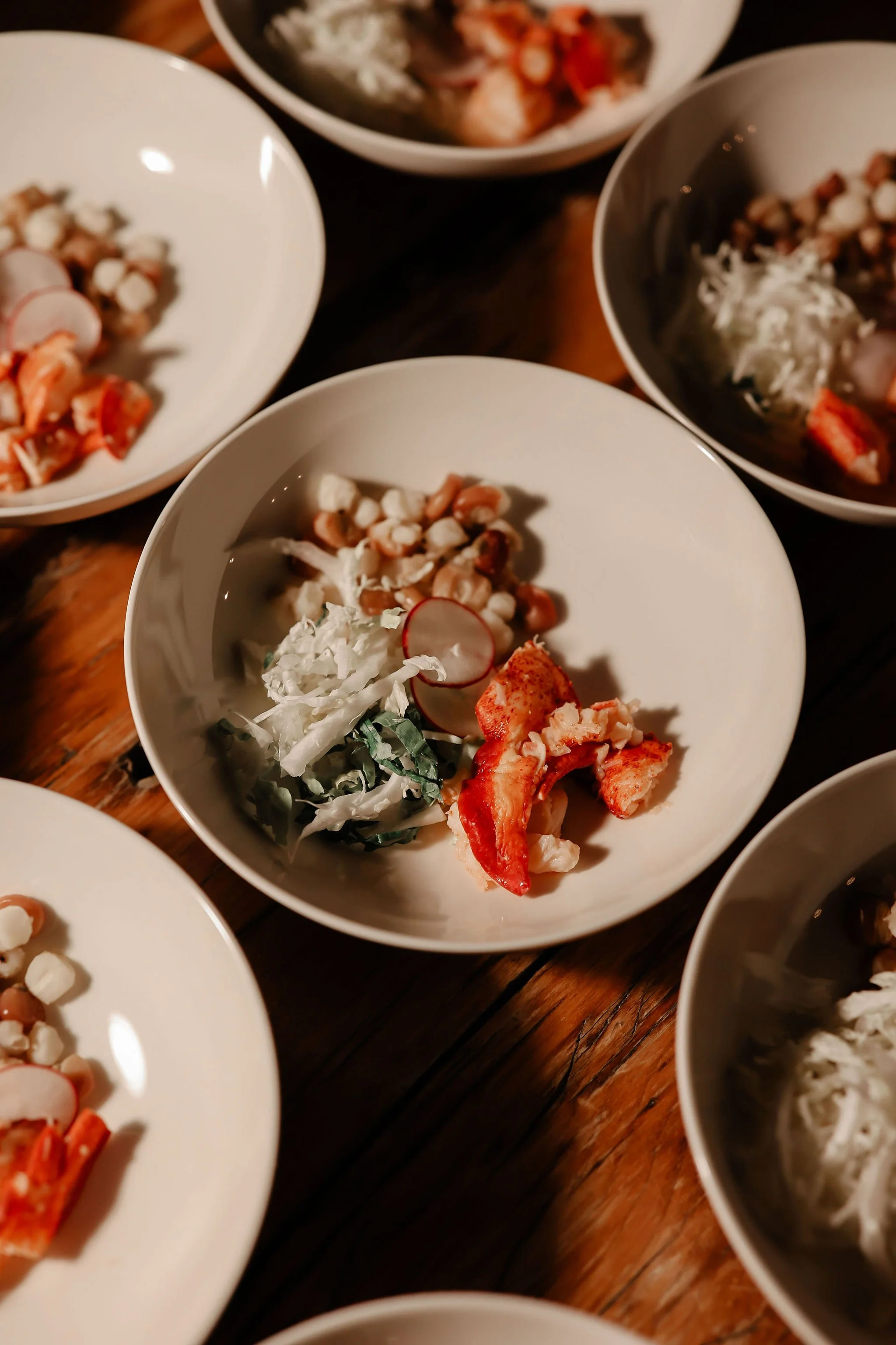 Multiple bowls of Asian-style appetizers on a wooden table, including seafood, vegetables, and garnishes.
