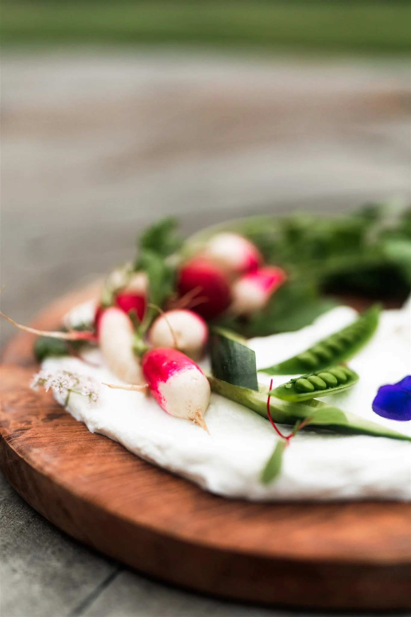 Close-up of fresh radishes, peas, and herbs on a wooden cutting board with a blurred background.
