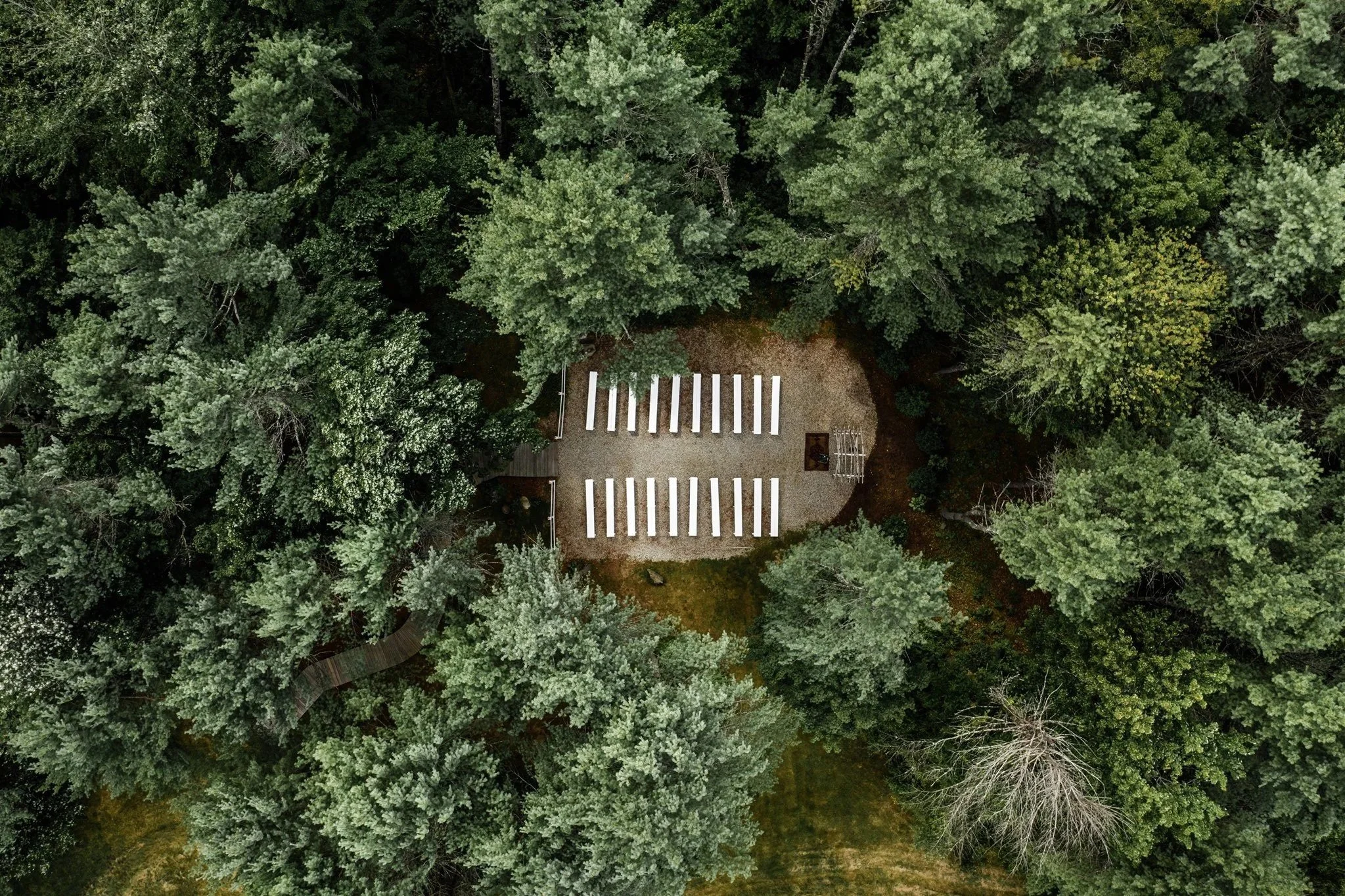 Aerial view of a small outdoor stage with white benches, surrounded by dense green trees.