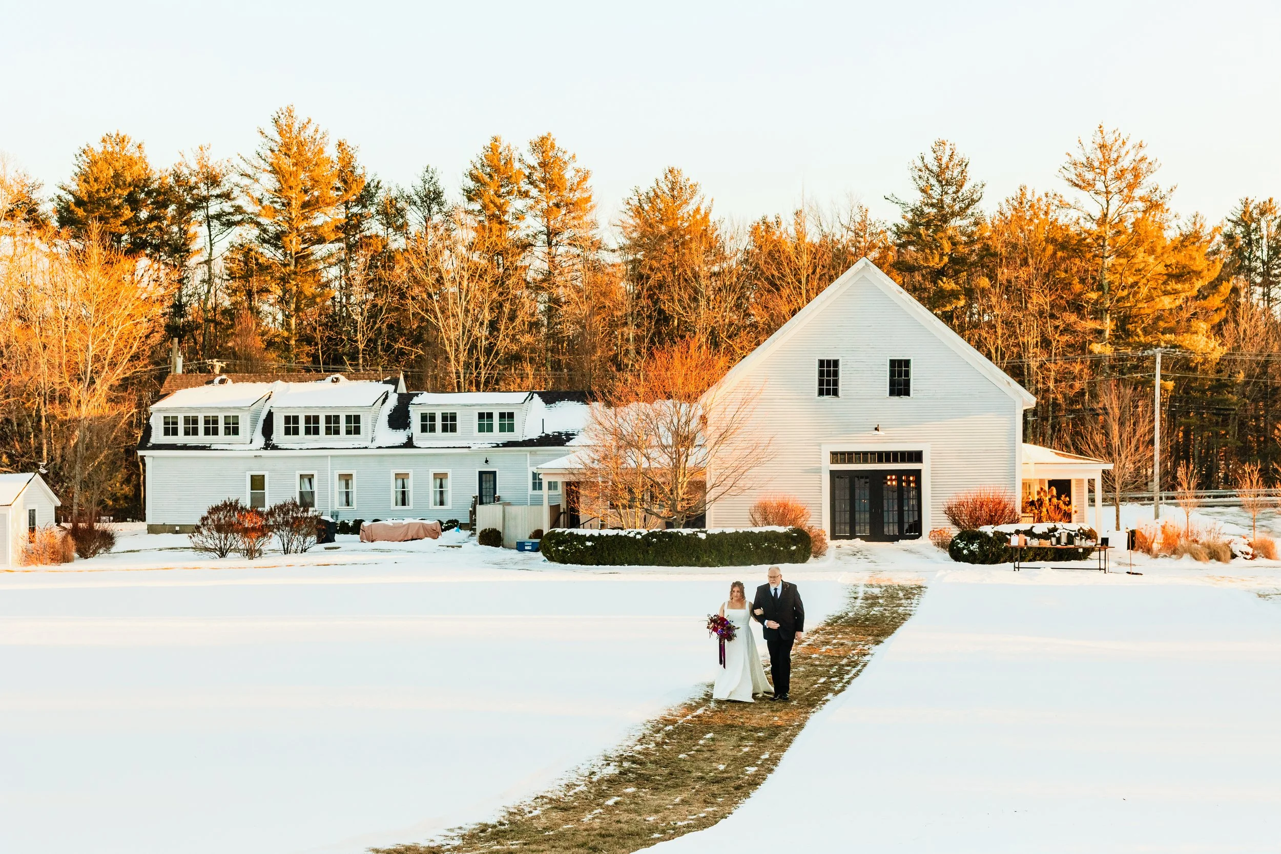 A bride walks down a snowy aisle outdoors at a barn wedding venue in maine