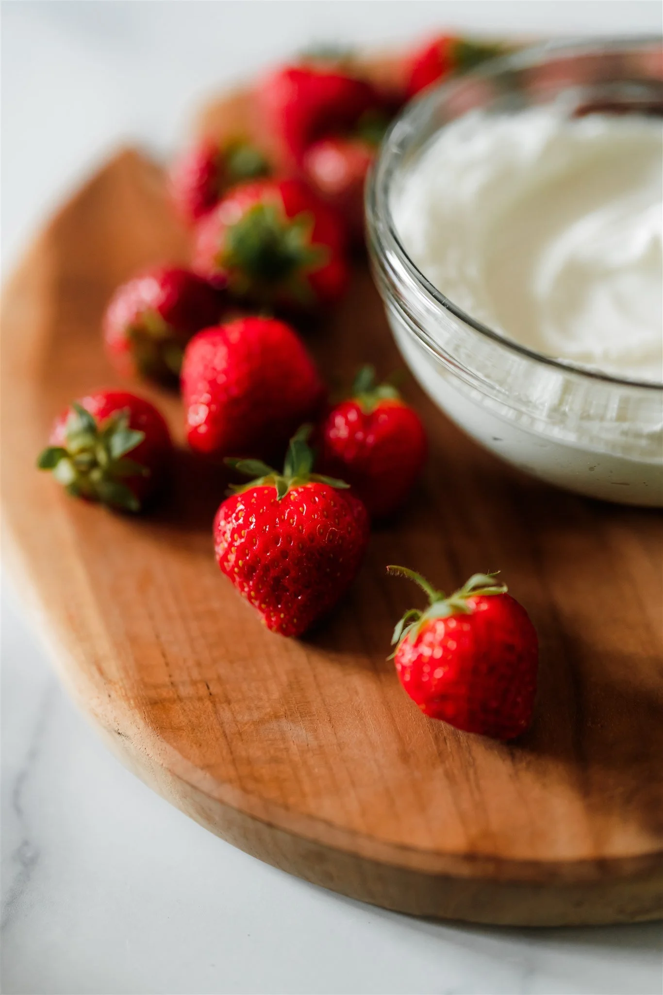 Fresh strawberries and a bowl of whipped cream on a wooden cutting board.