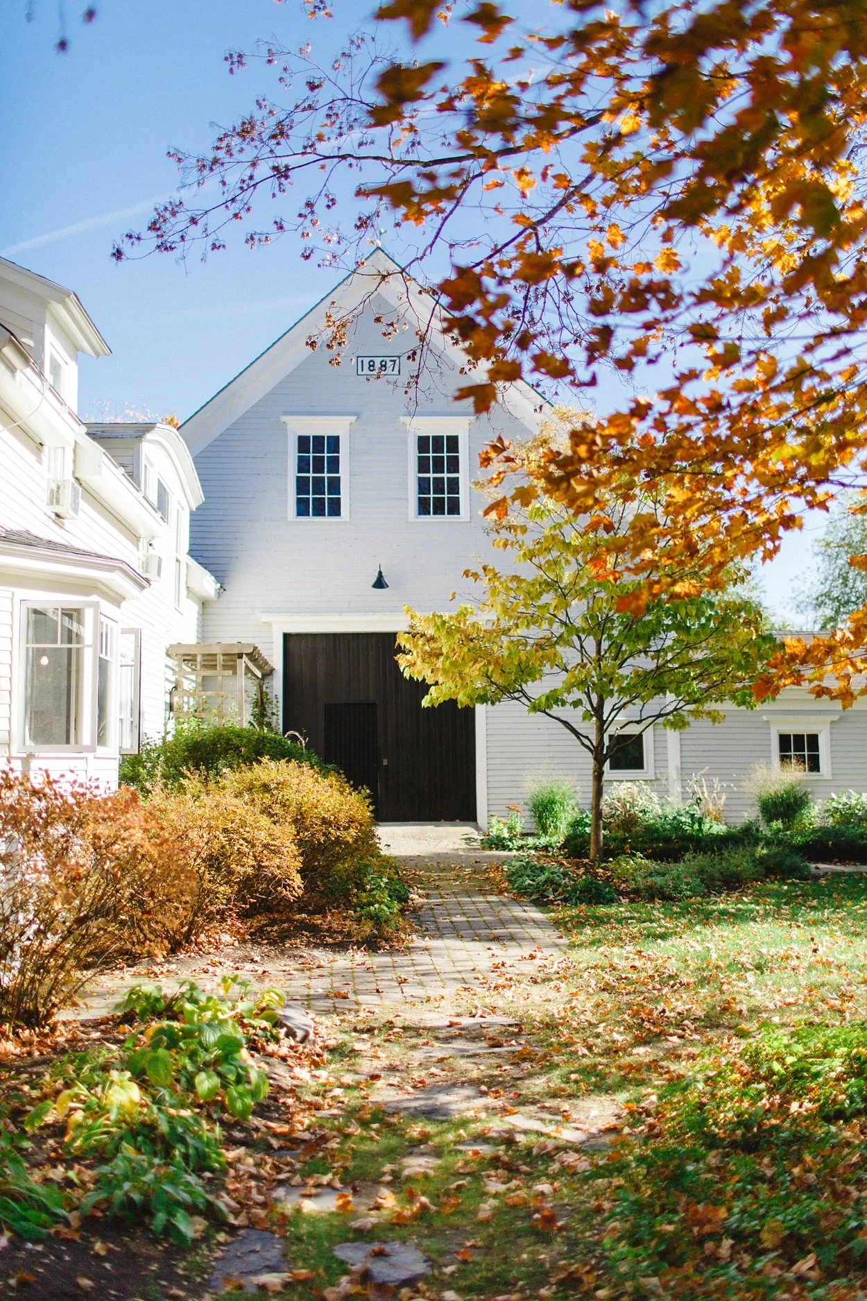 White house with black door, surrounded by trees with fall foliage, during daytime.