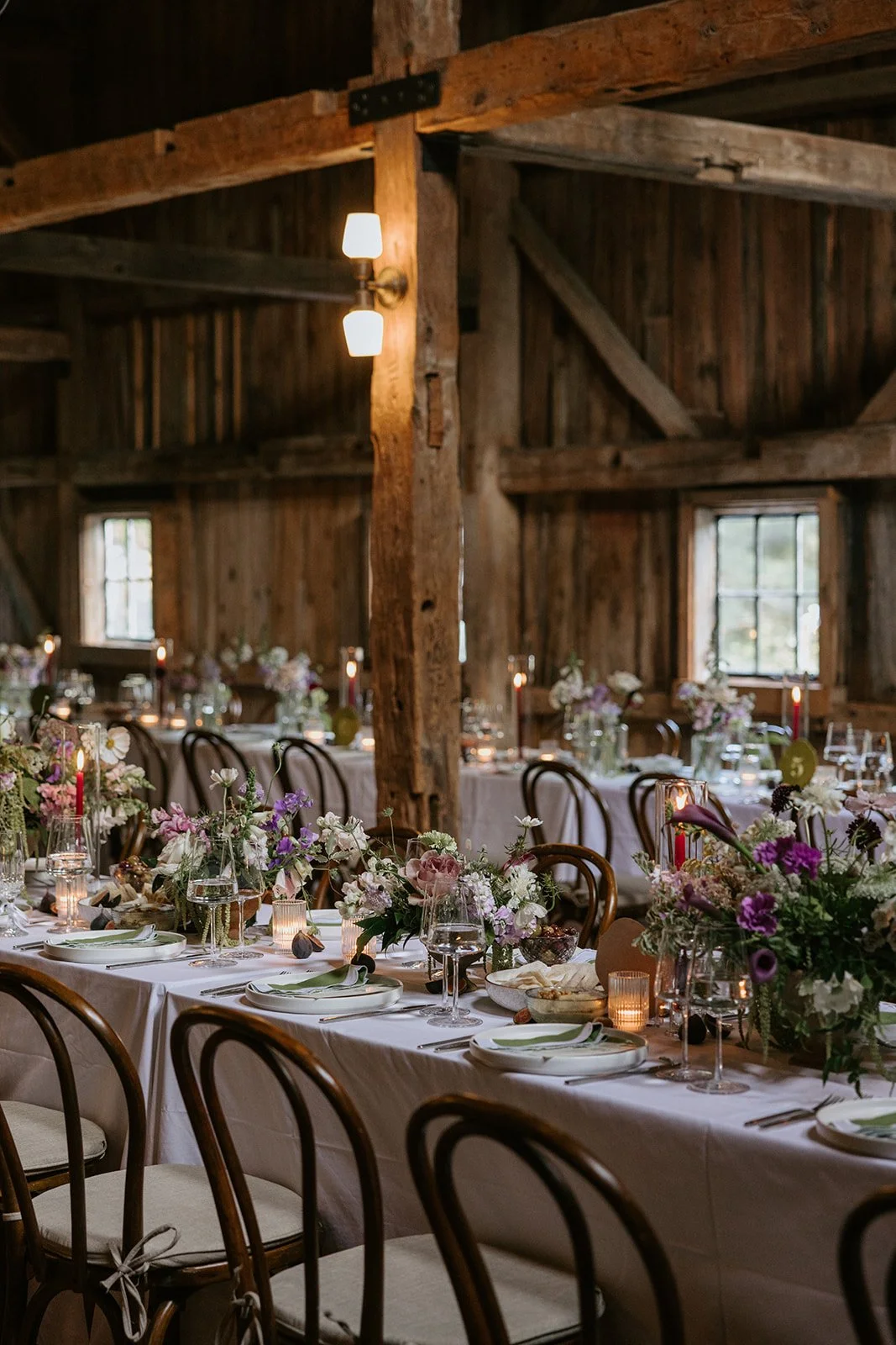 A rustic wooden banquet hall decorated for a wedding or special event with long tables, floral centerpieces, candles, and tableware.