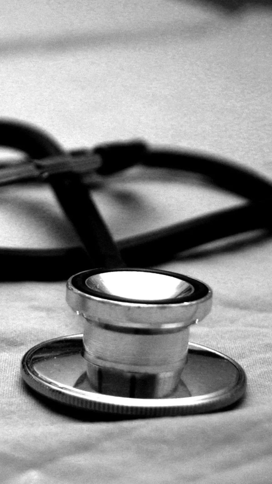 A close-up view of a stethoscope lying on a surface, with the chest piece in focus and the tubing extending out of the frame.