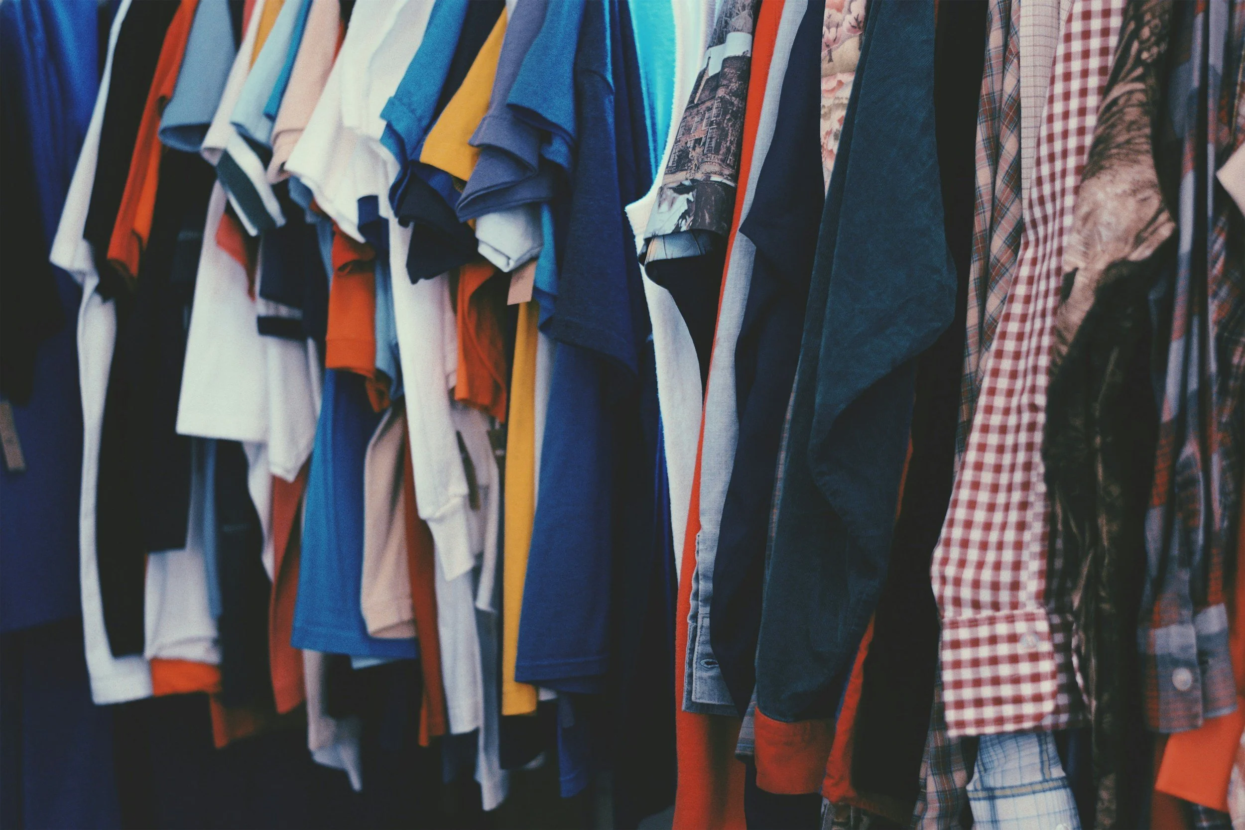 Clothes hanging on a rack, including t-shirts, shirts, and jackets in various colors and patterns.