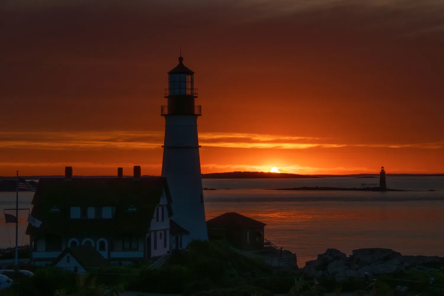 Portland Head Light on the rocky coast at sunset with a smaller lighthouse in the distance.