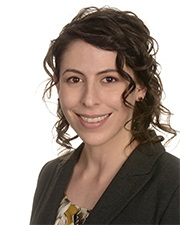 Headshot of a woman with curly brown hair, wearing a dark blazer, smiling at the camera.