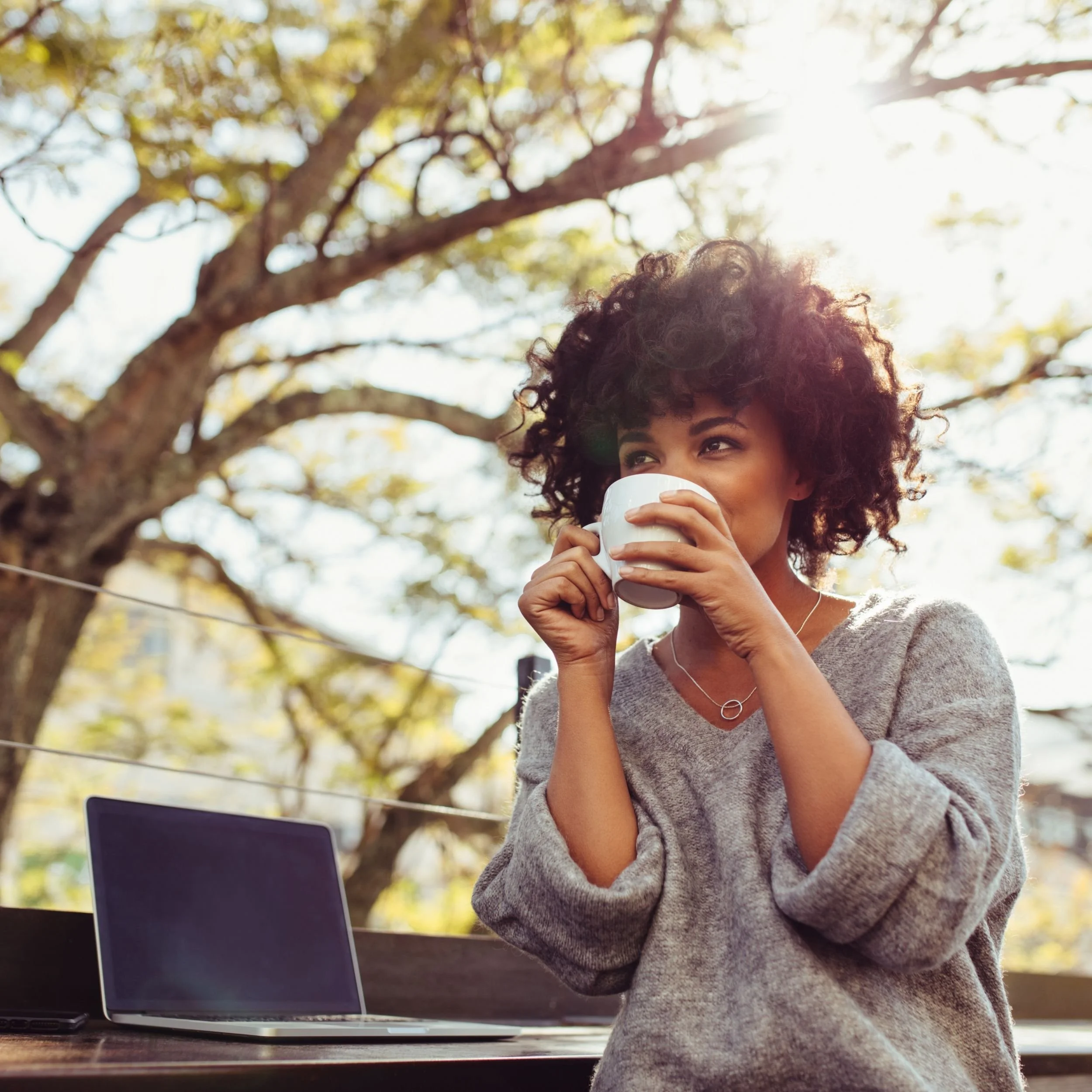 Woman enjoying coffee with laptop nearby
