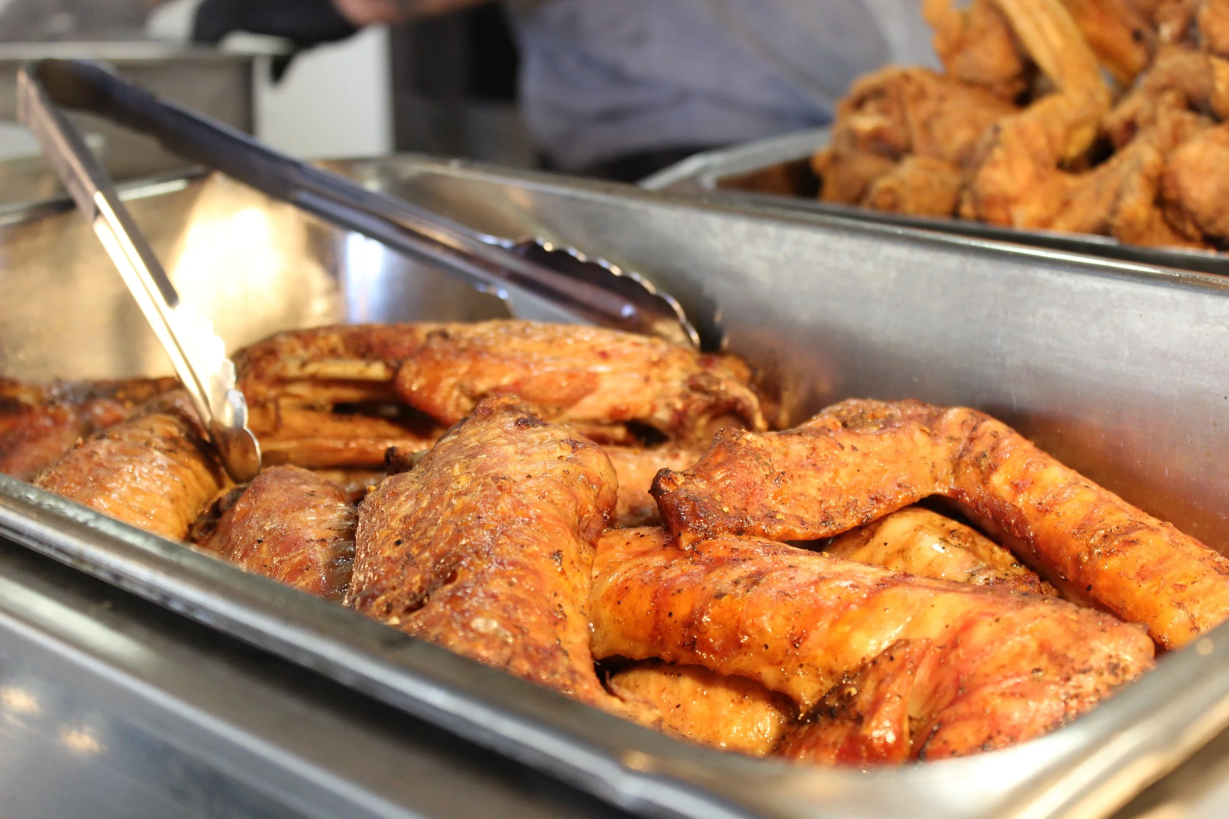 Tray of cooked seasoned chicken drumsticks in a stainless steel container.