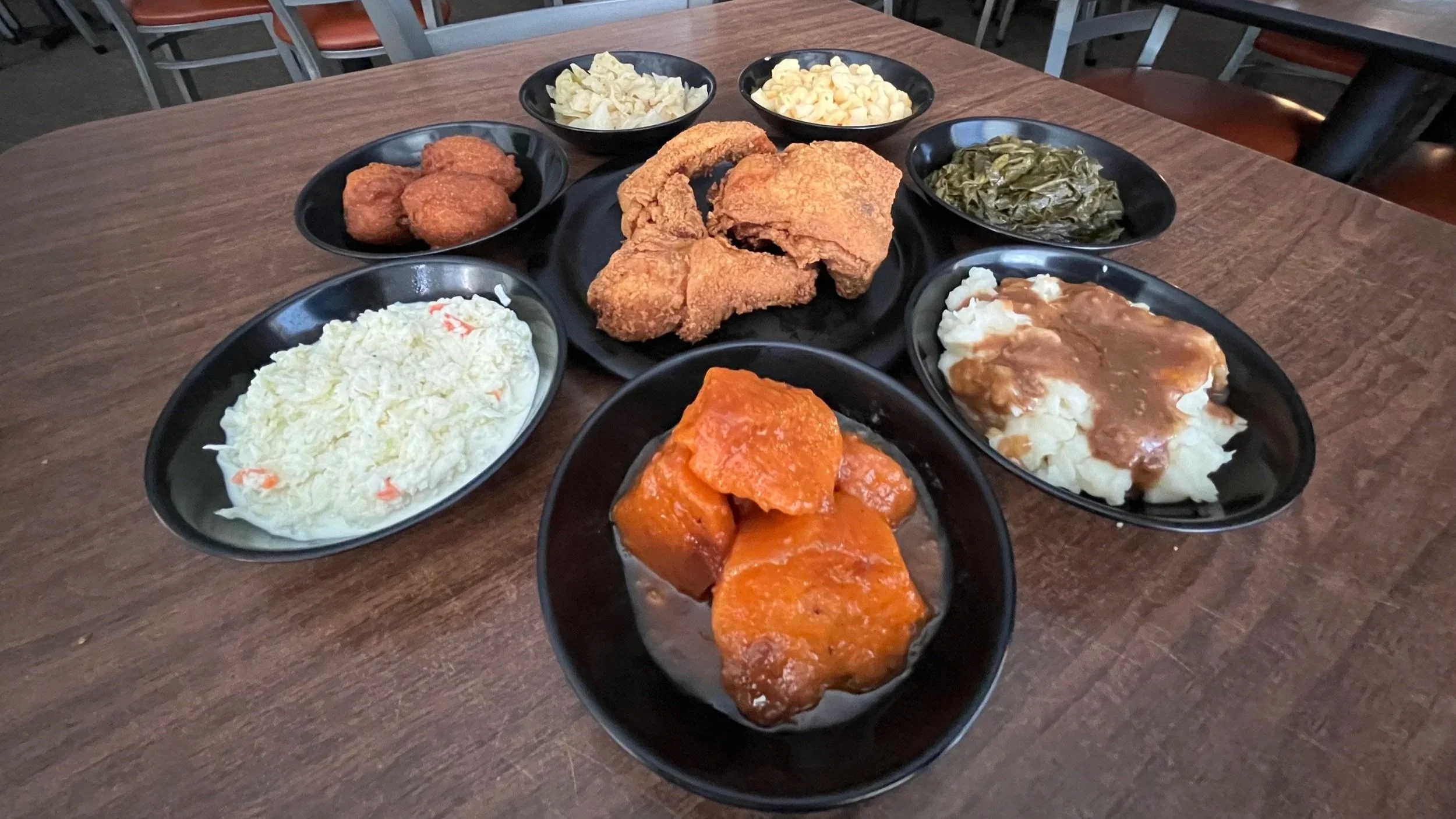 Various plates of Southern comfort food including fried chicken, collard greens, macaroni and cheese, mashed potatoes with gravy, sweet potatoes, and fried fish