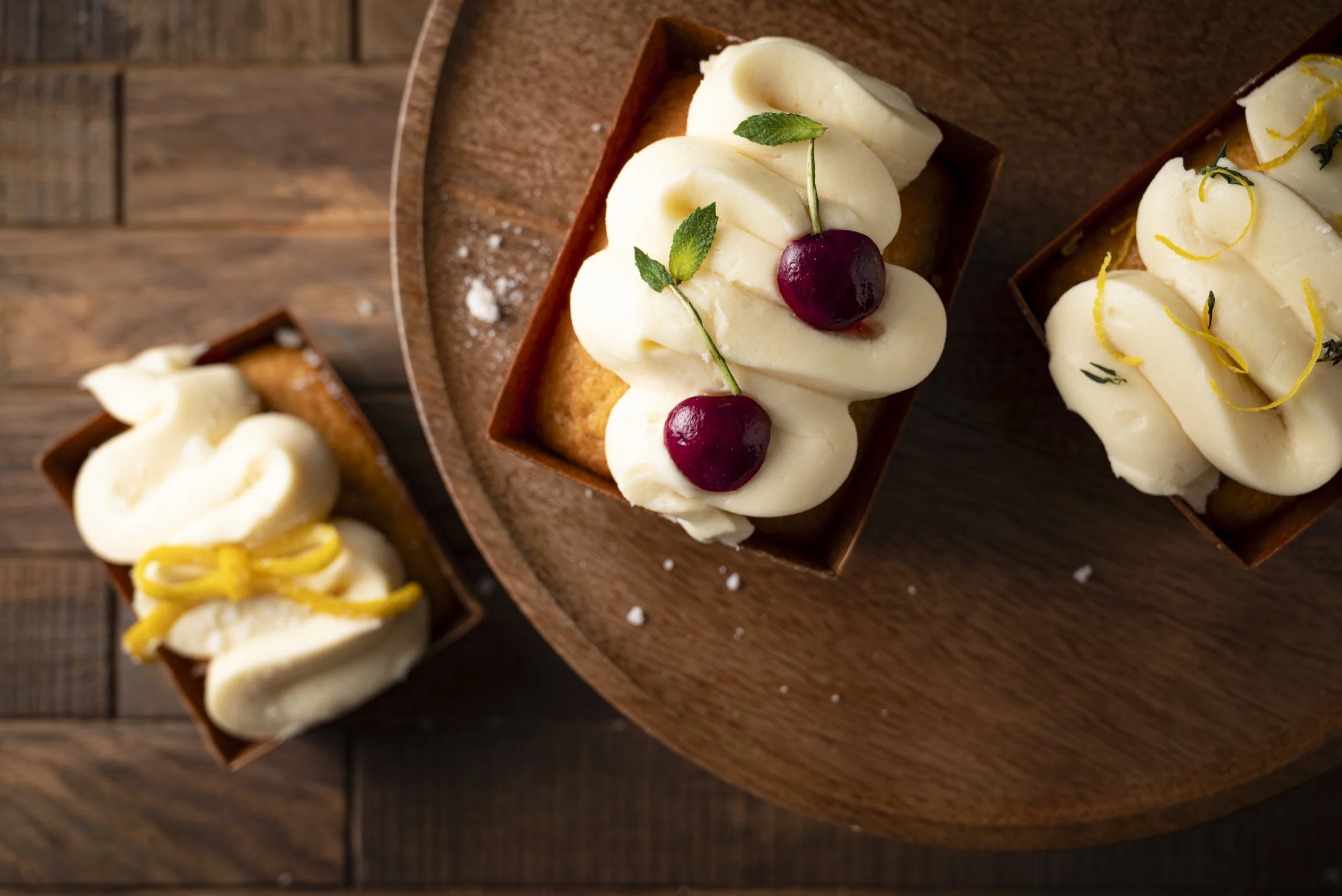 three minicakes with icing and fruit garnishes on wood backdrop.jpg