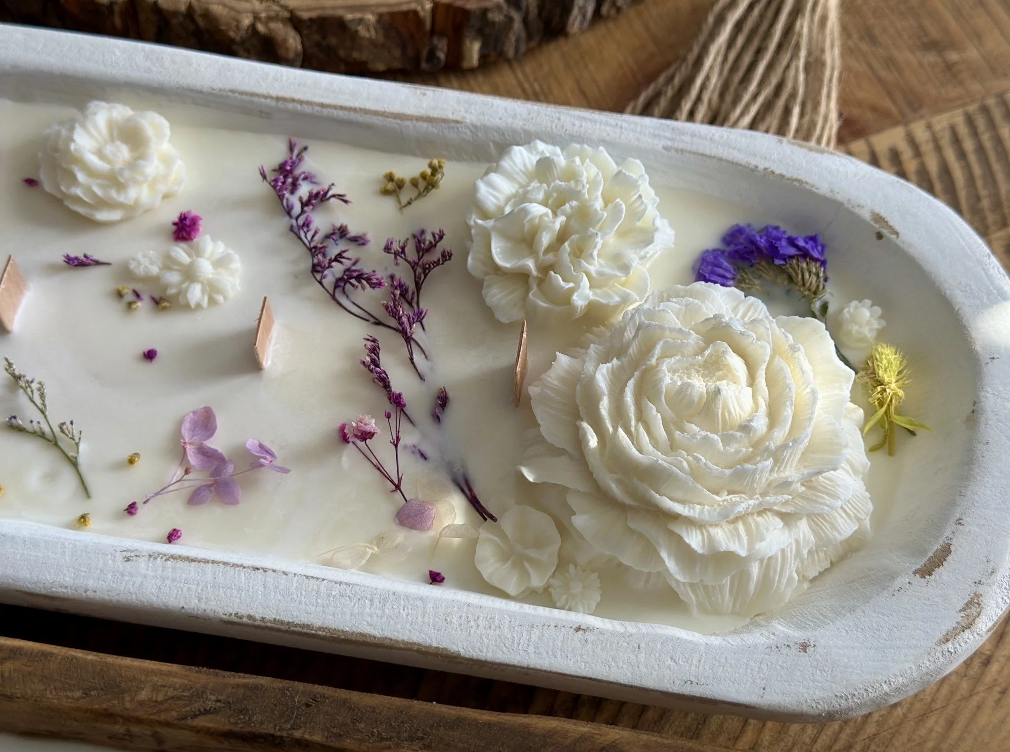 Decorative soap with white flower-shaped soap, dried flowers, and small purple, pink, and yellow flowers on a white tray.