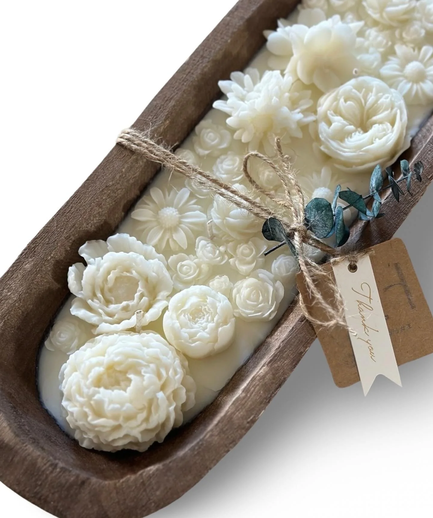 Cream-colored floral-shaped candles in a wooden tray, decorated with a twine bow and eucalyptus leaves, with a thank you tag attached.