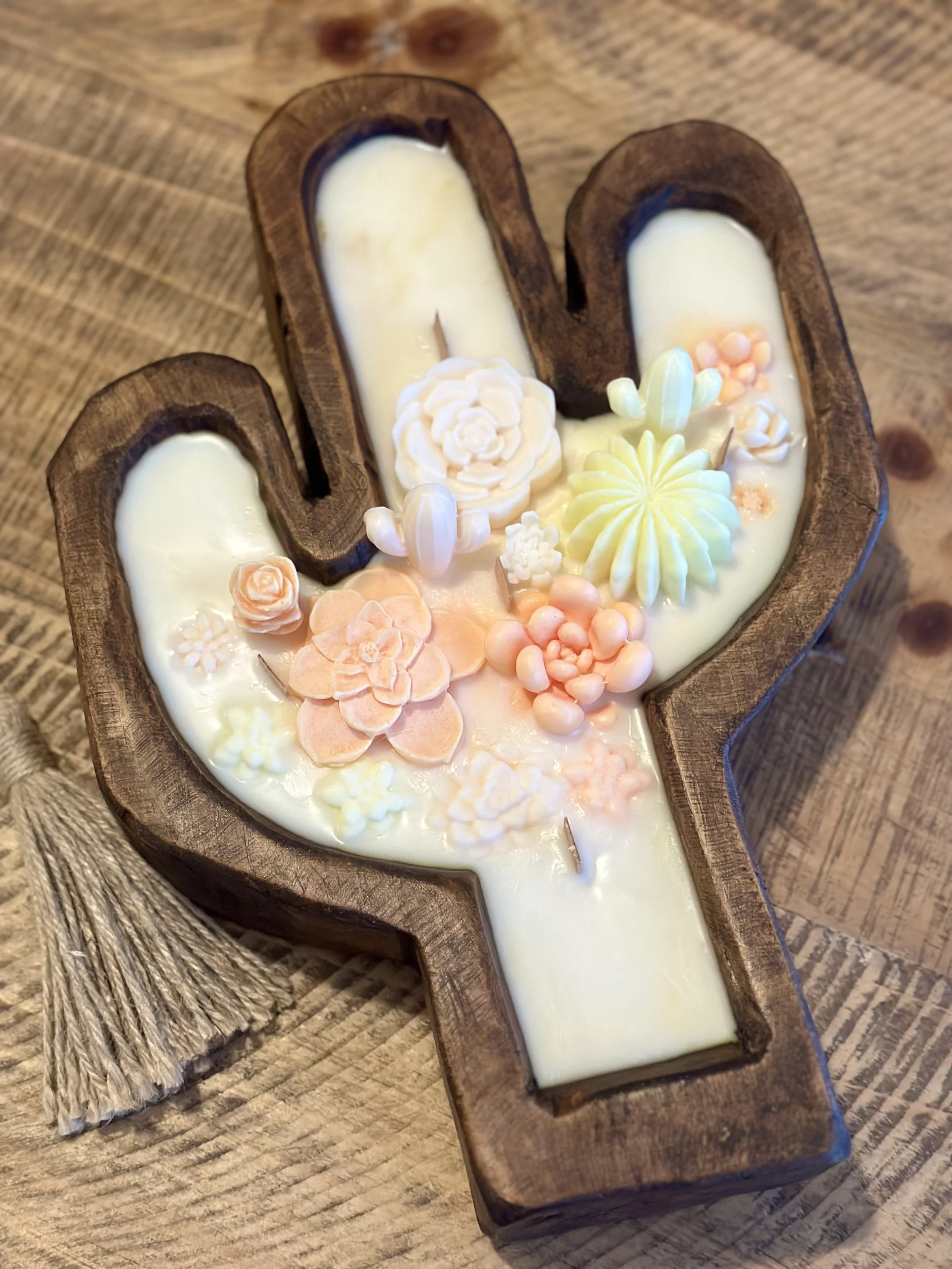 Decorative candles inside a wooden cross-shaped holder, adorned with pastel-colored floral and floral-like shapes.