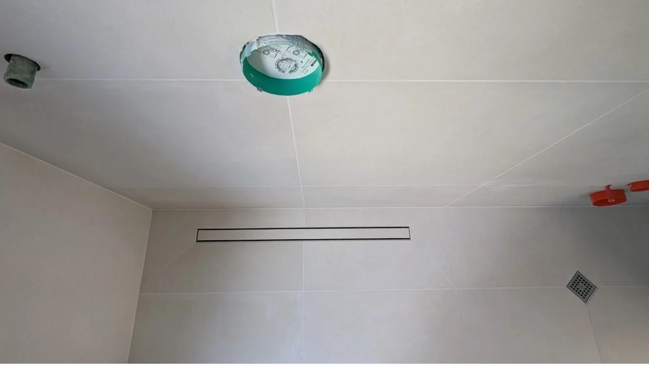 Ceiling of a room with a holes for light fixtures, with one light fixture missing, and a ventilation grate. The photo is taken from below, looking up at the ceiling.