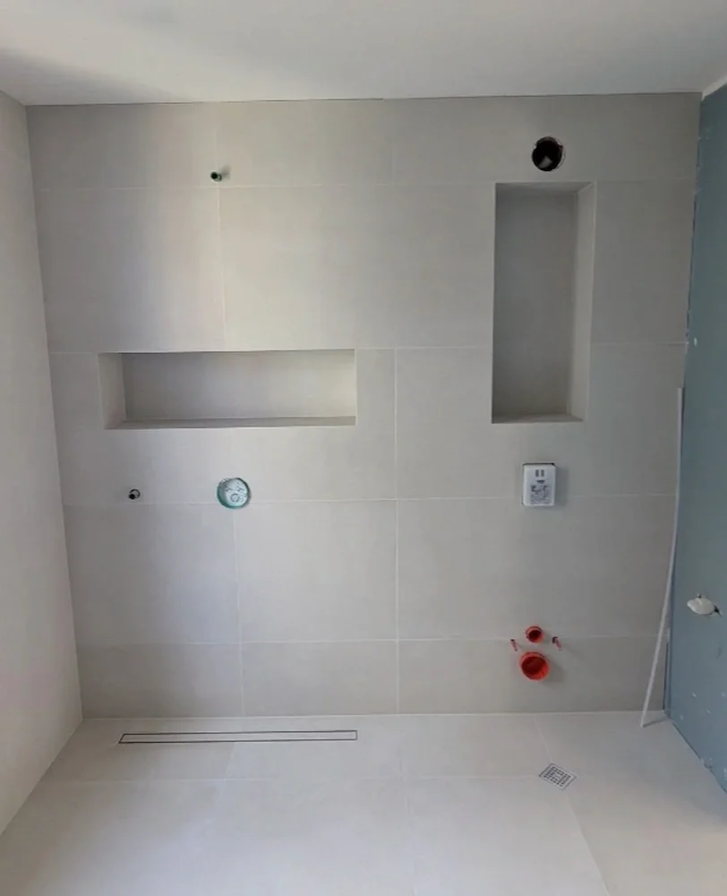 Bathroom wall with recessed shelves, plumbing fixtures, and an exhaust vent under construction.