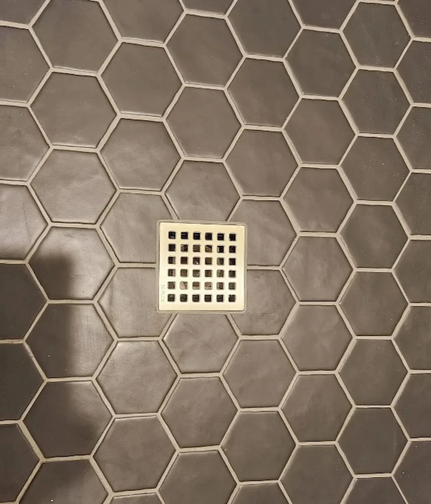 Gray tile floor with a square drain in the center.