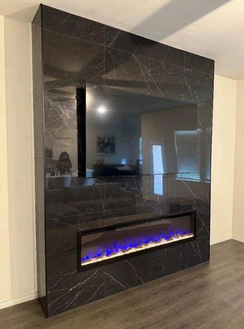 Black marble wall with a built-in electric fireplace and a mounted flat-screen TV, inside a living room.