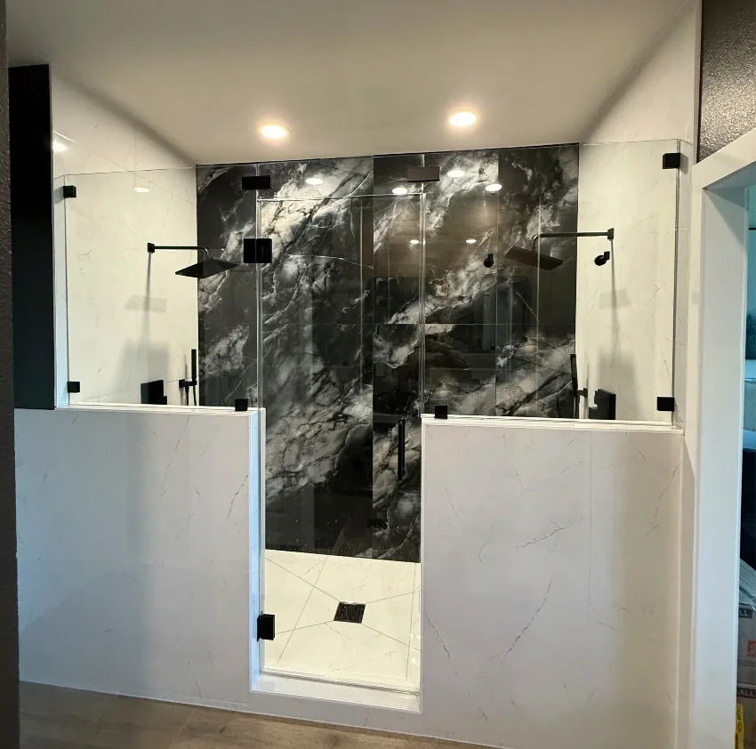 Modern shower with clear glass enclosure, black marble walls, and white marble half-walls.