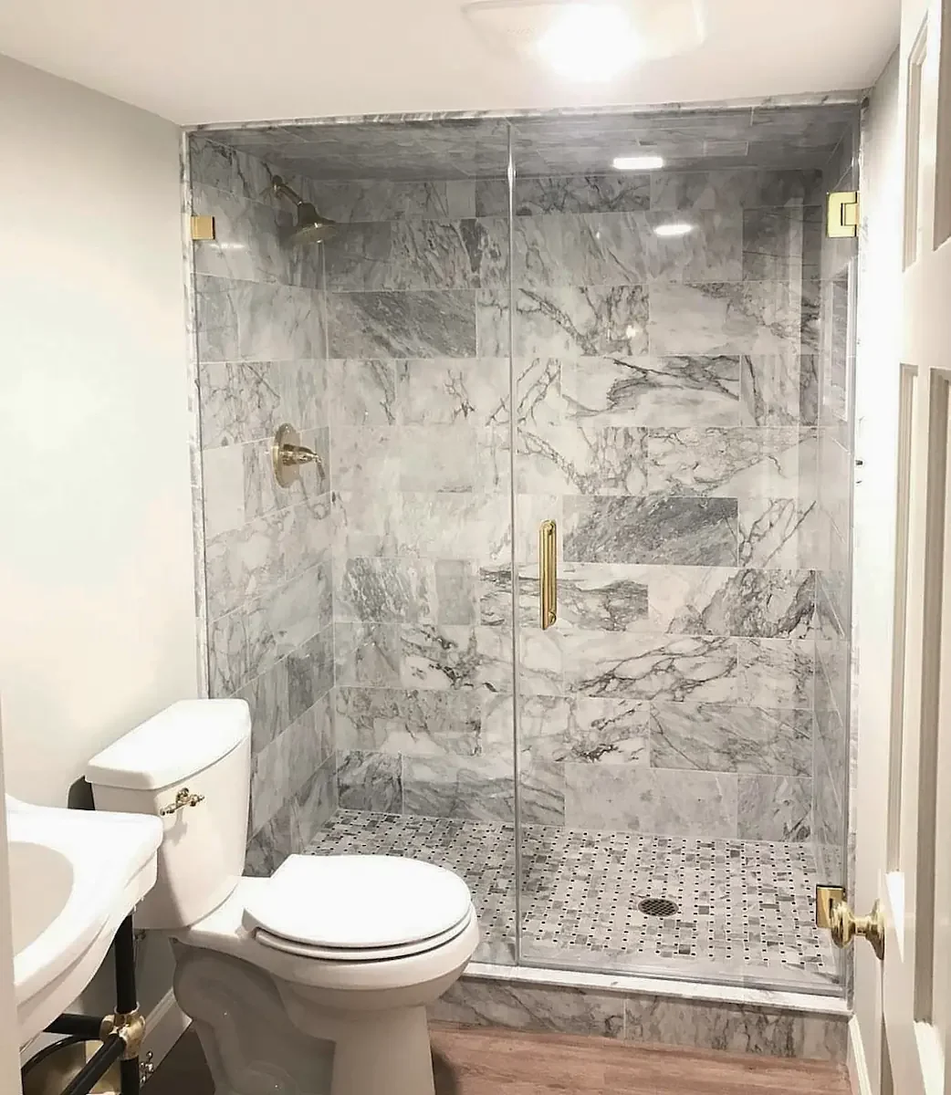 A modern bathroom with a glass-enclosed shower featuring marble tiles, a white toilet, and a white sink.