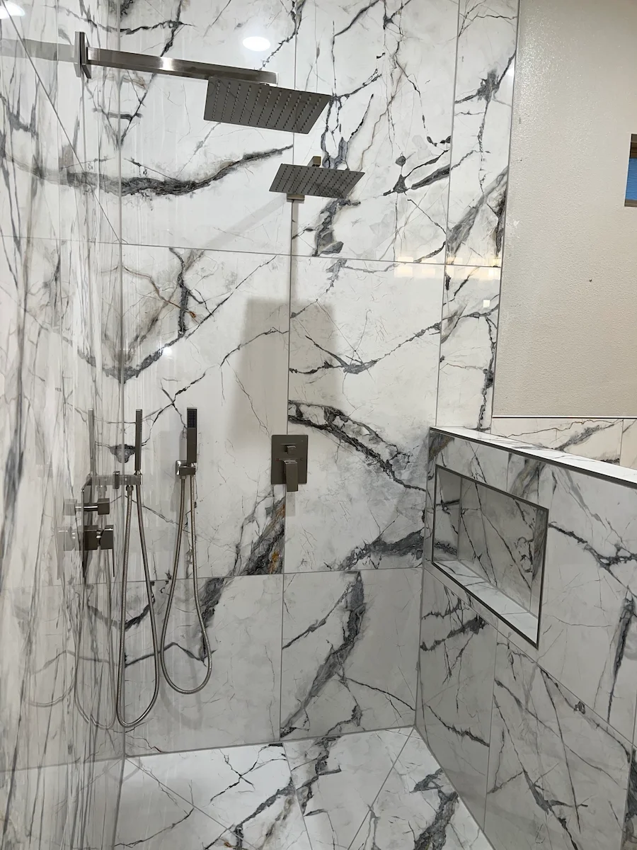 Marble shower with two showerheads, a built-in shelf, and a wall-mounted control panel.