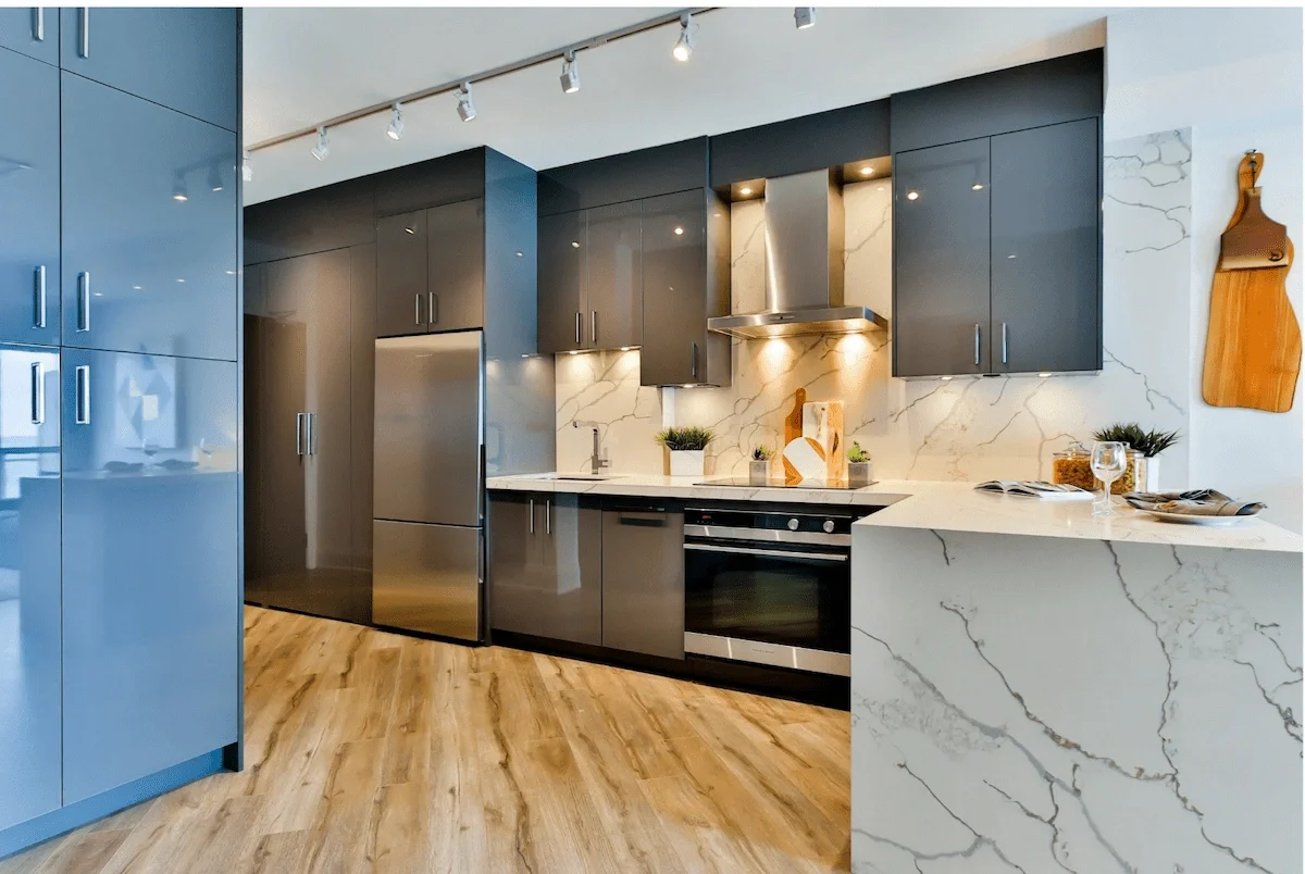 Modern kitchen with dark gray cabinets, stainless steel refrigerator and oven, marble backsplash, and wood flooring.