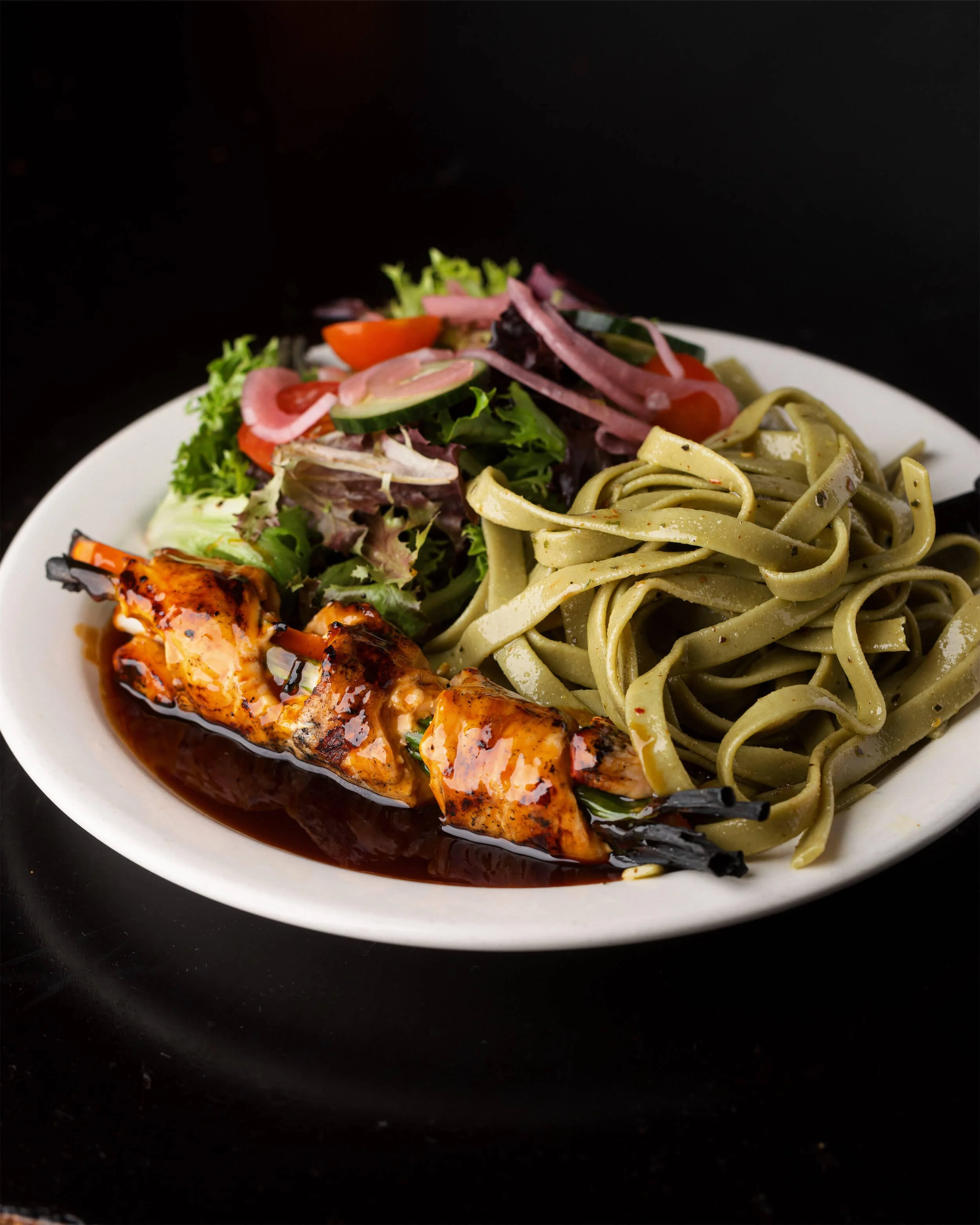 Plate of cooked pasta with green sauce, a salad with mixed greens and vegetables, and grilled chicken skewers in barbecue sauce at Ryan's Wake | An Irish Pub, Bar & Restaurant in Troy, NY with River Views, Outdoor Seating & Live Music