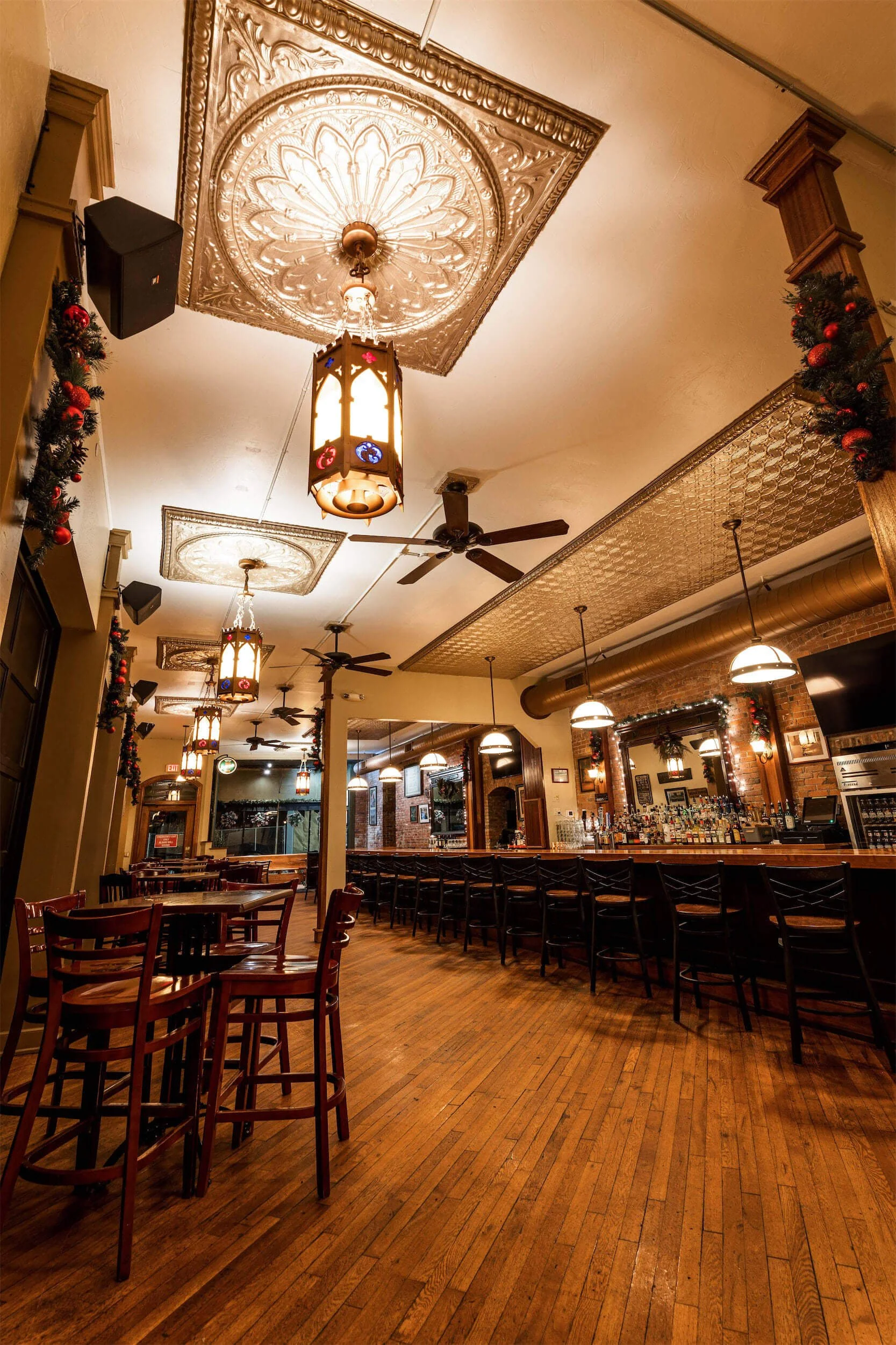 Interior of Ryan's Wake in Troy, NY, with wooden floors, a long bar counter with barstools, hanging lights, ceiling fans, and ornate ceiling details.