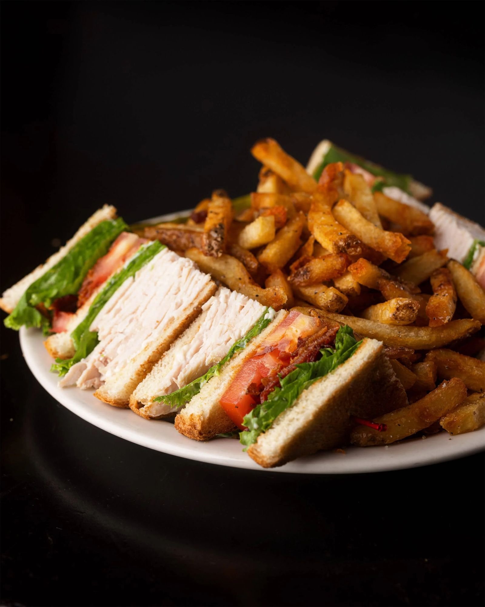 Turkey Club Sandwich at Ryan's Wake, stacked with turkey, bacon, lettuce, and tomato on toasted white bread, with house-cut fries.