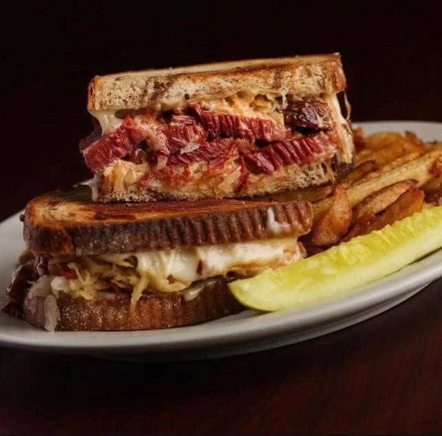 Close-up of a plate with a double-stack grilled cheese sandwich cut in half, revealing melted cheese, sliced meats, and bread, accompanied by French fries and a pickle spear at Ryan's Wake | An Irish Pub, Bar & Restaurant in Troy, NY with River Views