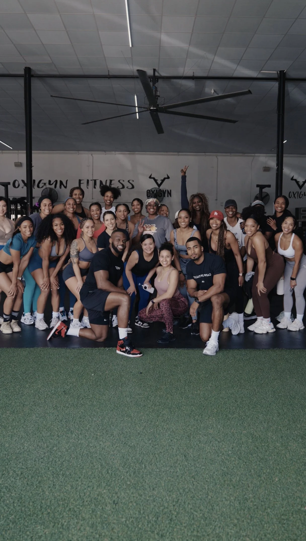 Coach Osamoje walking outdoors with a group of smiling clients wearing Grow With O shirts, showcasing community, positivity, and teamwork in fitness.