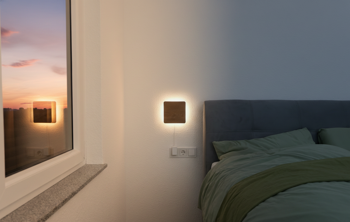 A bedroom with a window, wall-mounted light, and bed with green bedding.