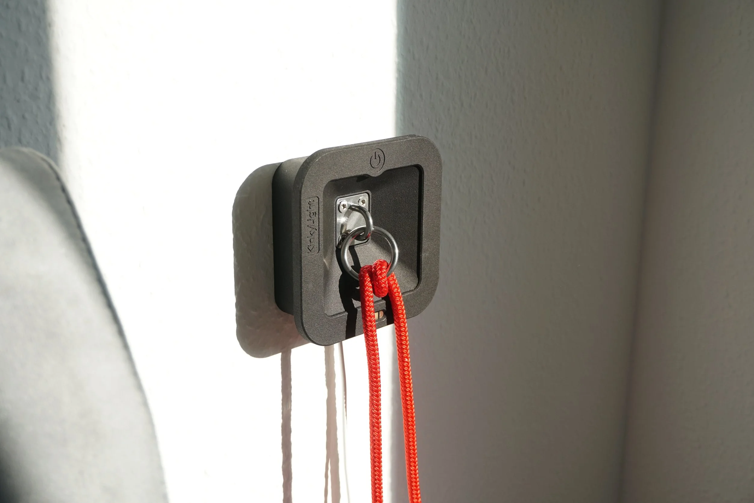 A wall-mounted bedside lamp with the cover remoed, a metal ring in the center, and two red ropes hanging from the ring.