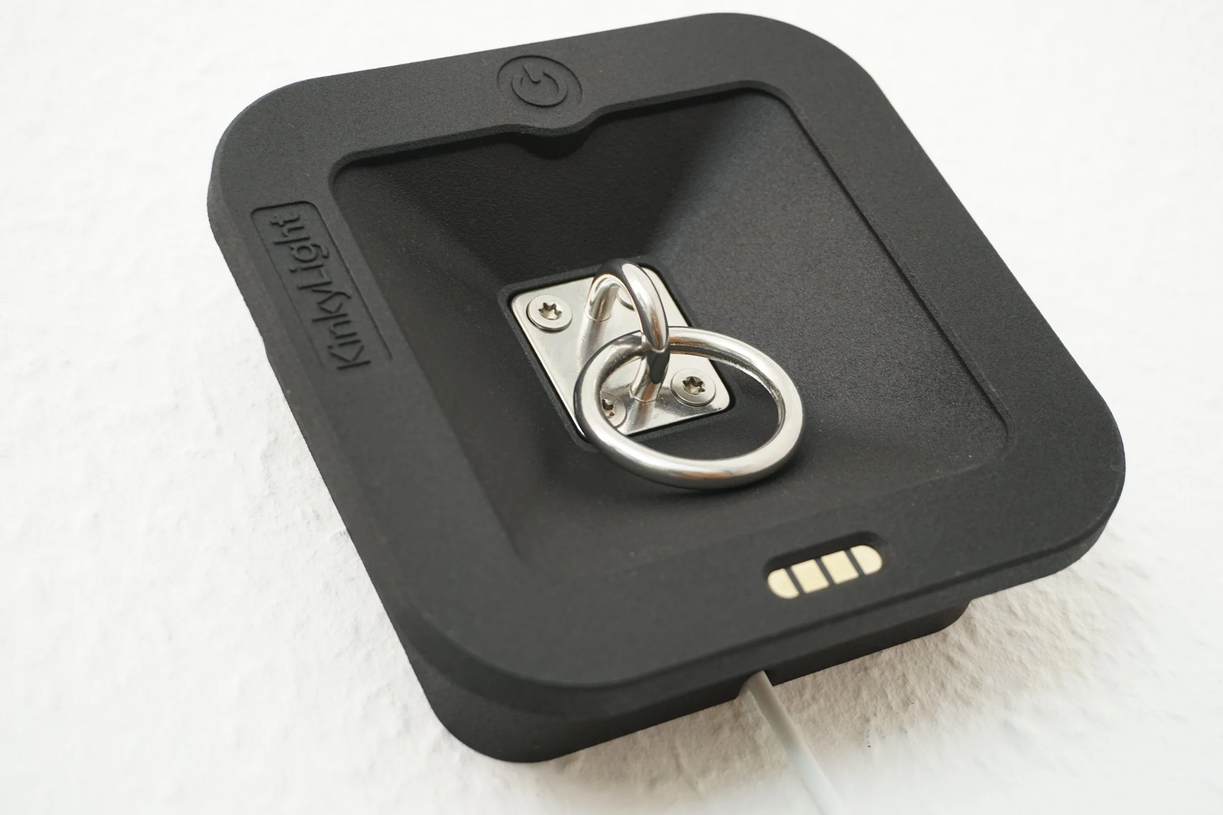 A close-up of a black wall-mounted bedside lamp light switch with a metal ring pull handle in the center, mounted on a white wall.