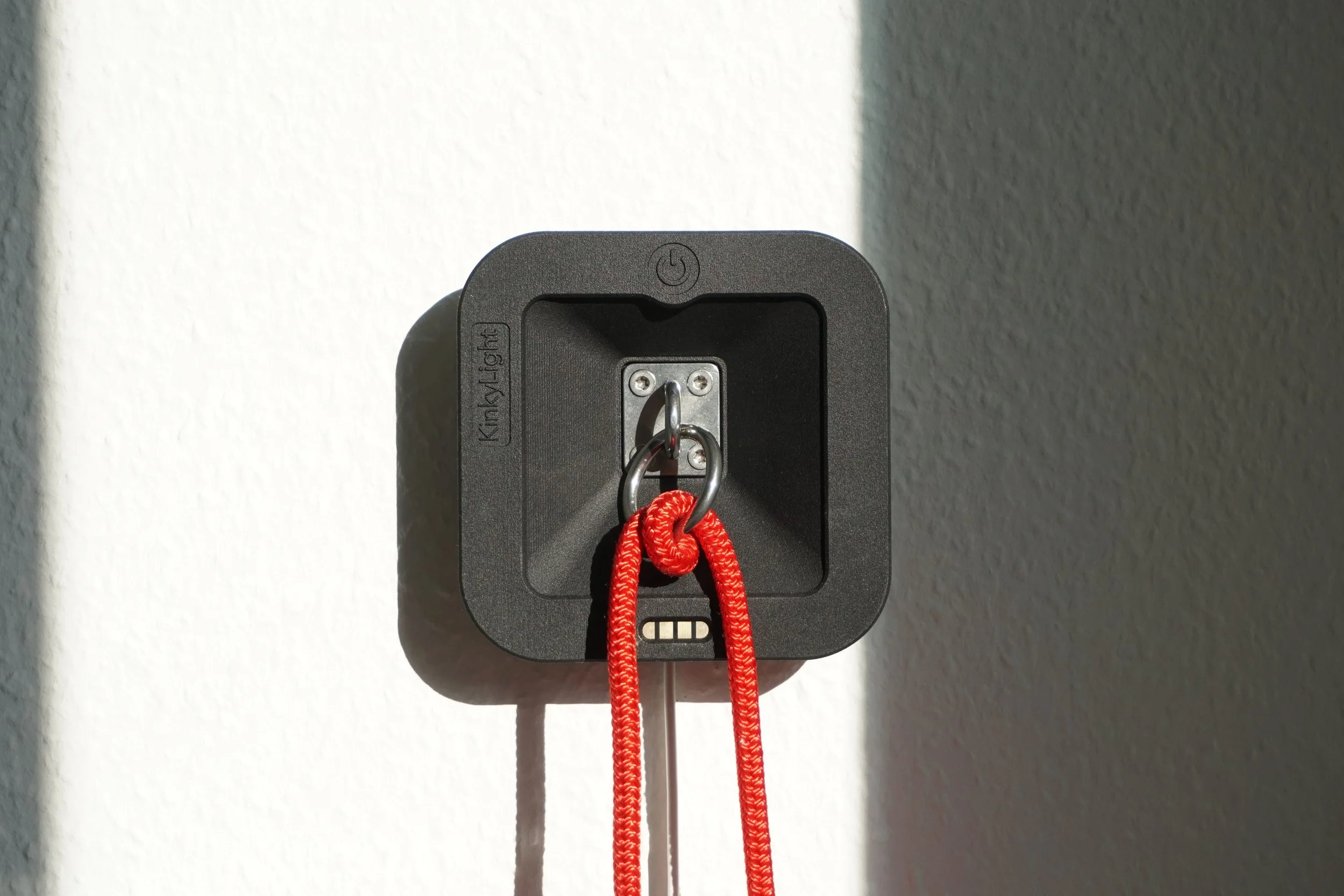A close-up of the KinkyLight bedside lamp with a metal ring in the center, with a red rope attached to the ring.
