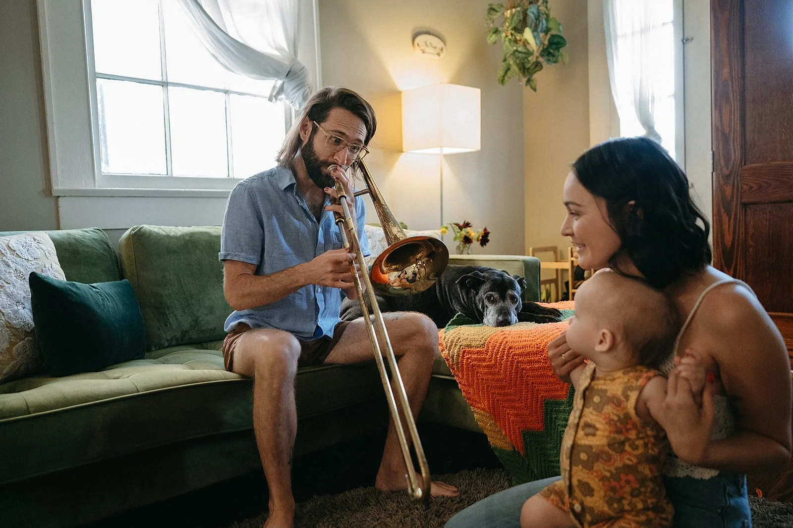 Dad playing the trombone for mom and son during their in home family photo session, New Orleans