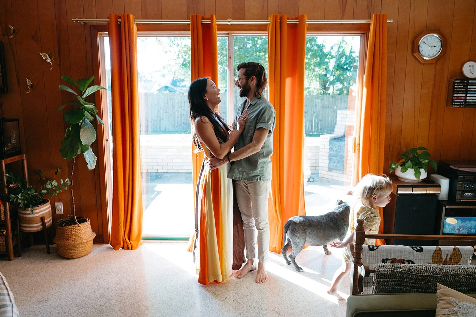 Mom & dad standing in living room while their son runs around the room during their in home family session