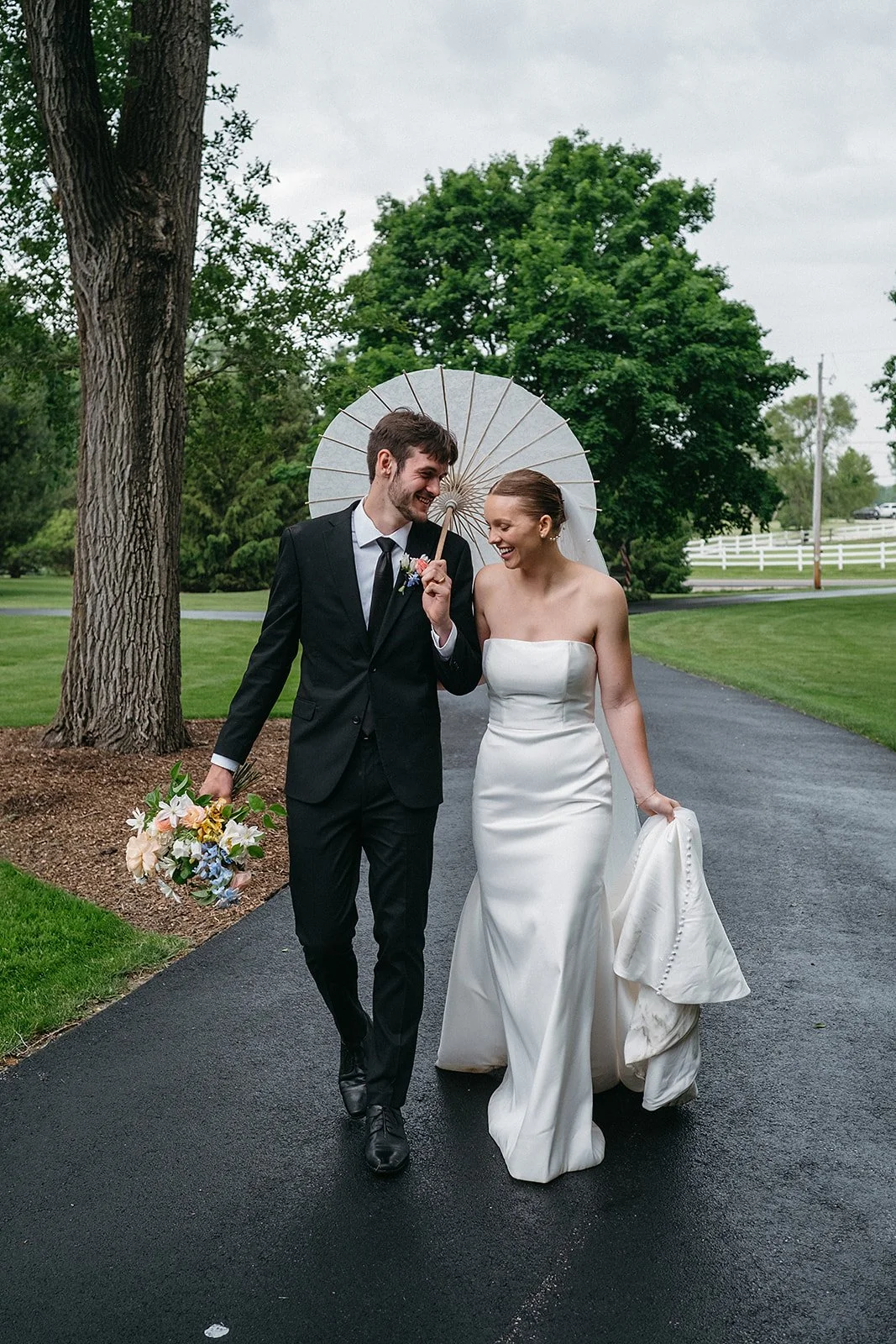 Bride and groom walking away from their wedding ceremony.  Under an umbrella with wedding dress and bouquet. 