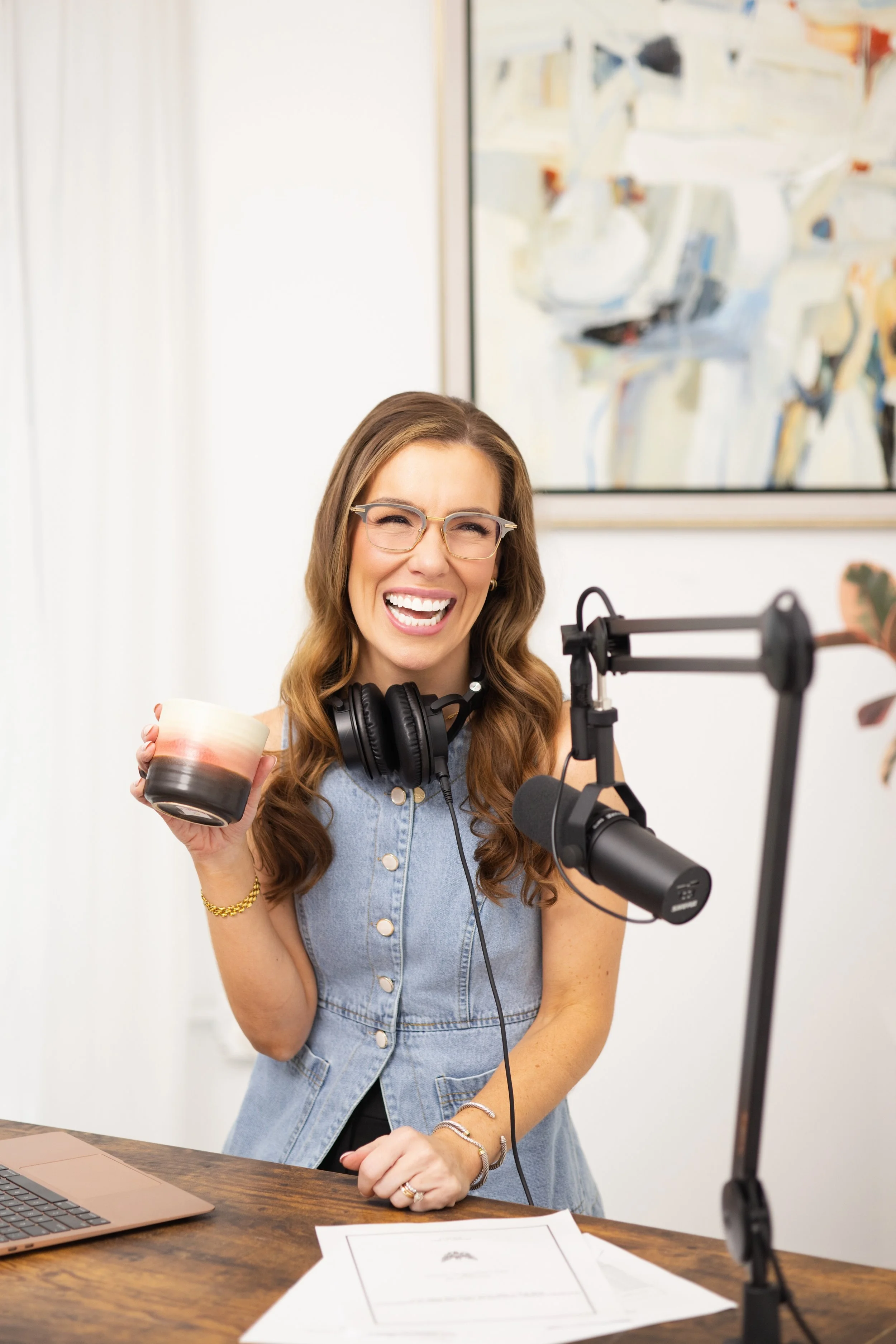 Mattie holding a coffee cup in her podcast studio with podcast headphones and a podcast mic