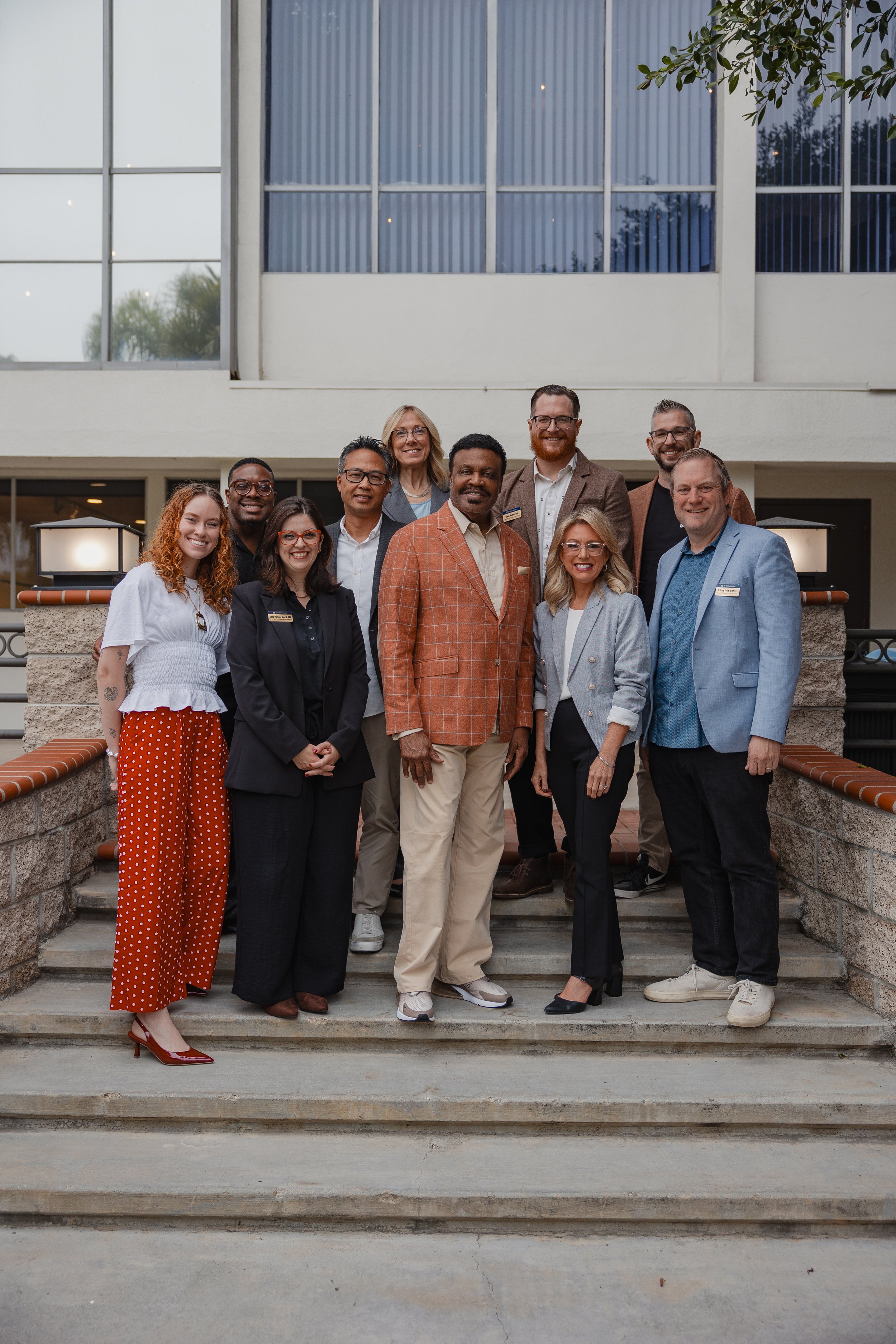 Group of the MPI Conferences speakers and leaders standing on steps outside a modern building, smiling at the camera.