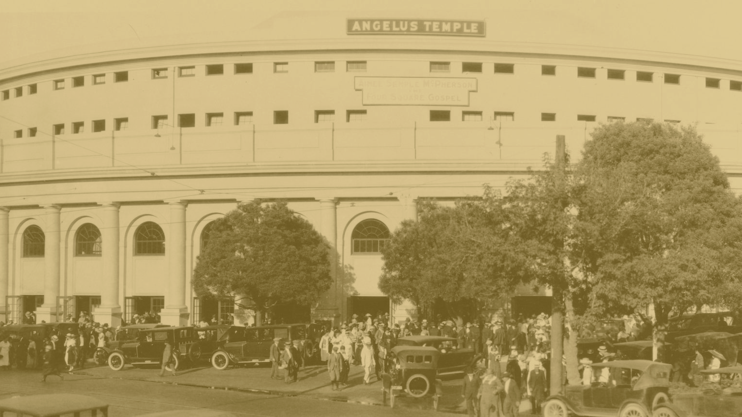 Historical photo of the Angelus Temple with a crowd of people and vintage cars in front of the building, which is labeled with the sign "Angelus Temple" at the top.