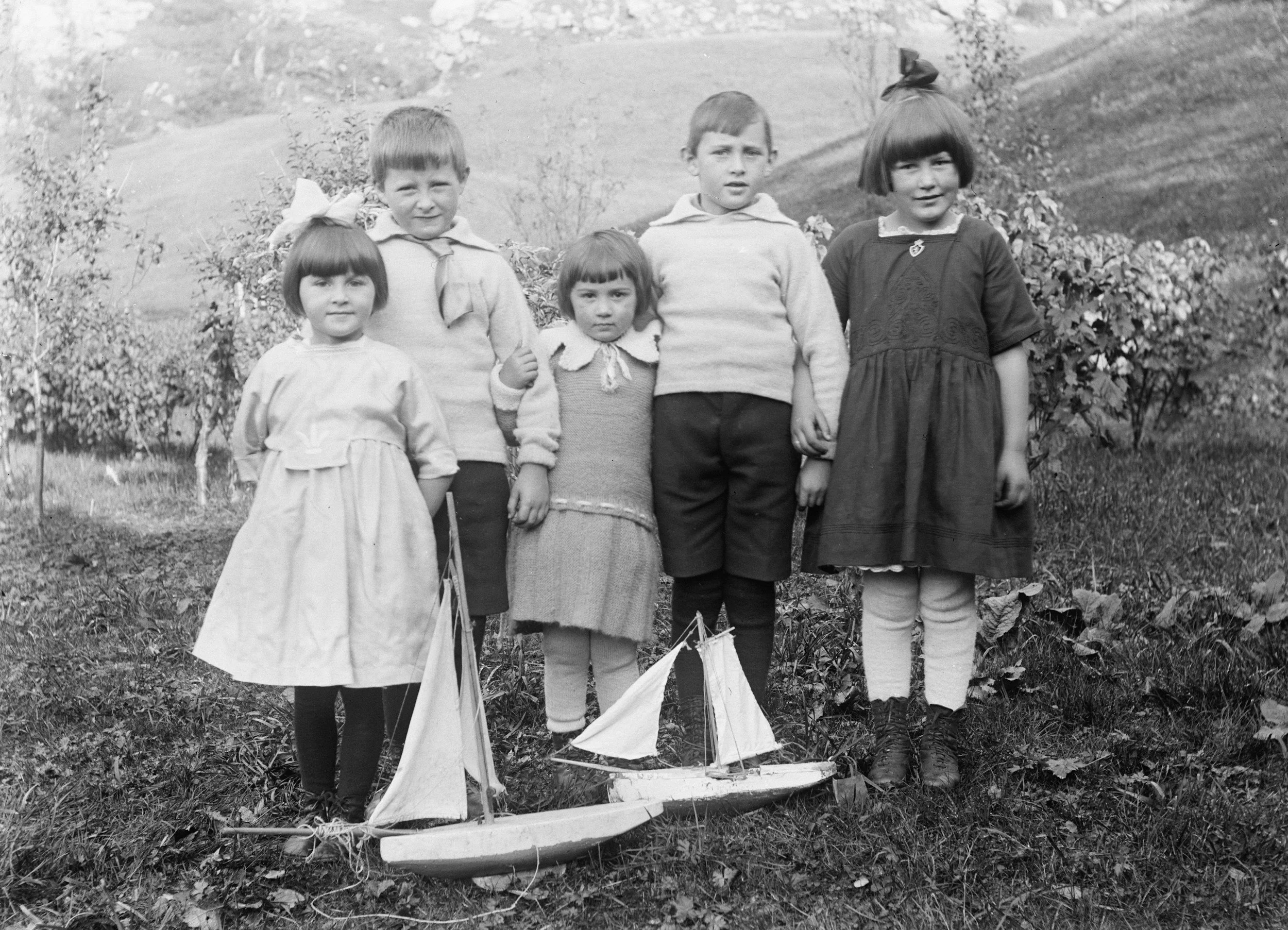 Groupe de six enfants posant dans un jardin avec deux petits bateaux en bois.