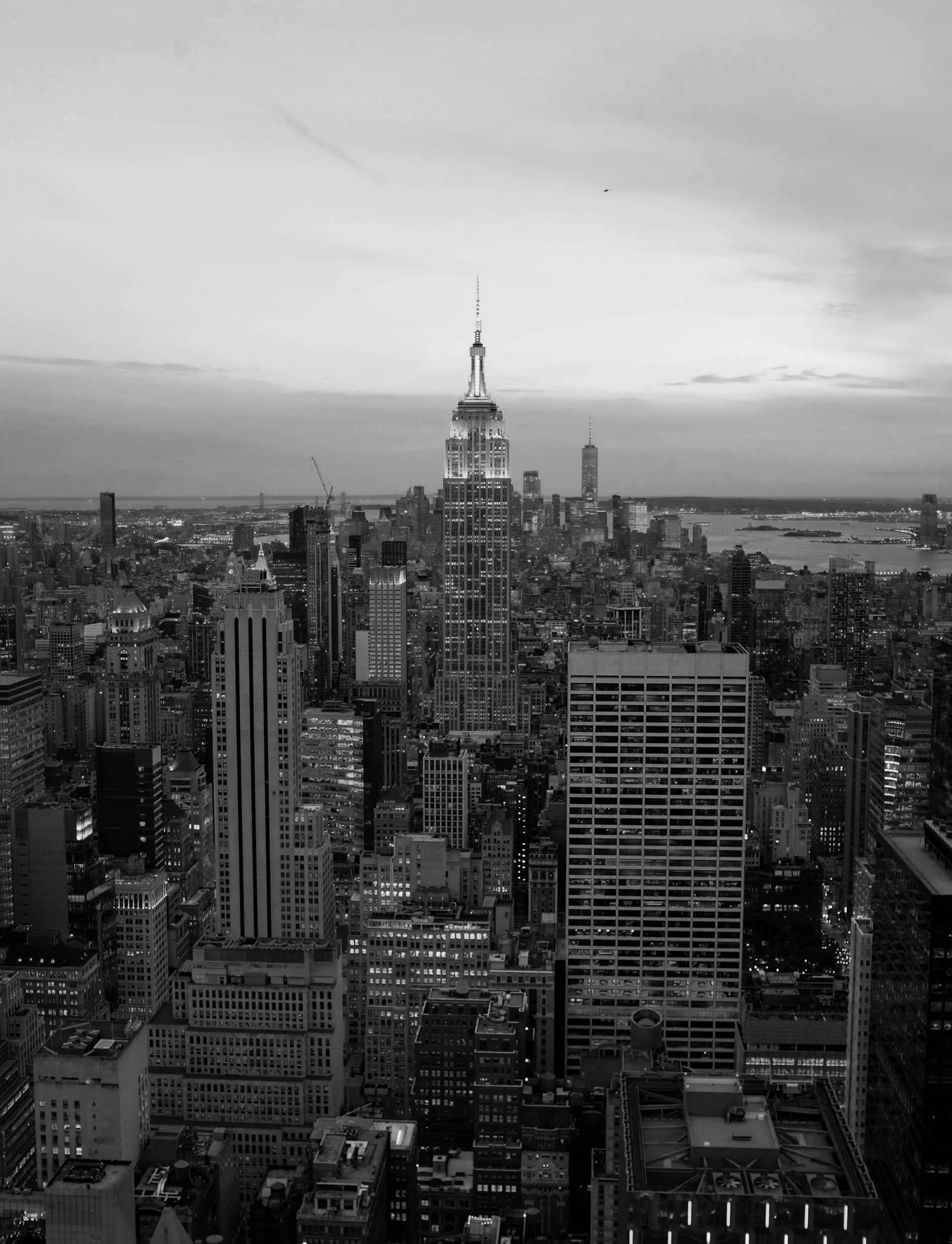 Black and white aerial view of New York City skyline with the Empire State Building prominently in the center, surrounded by tall skyscrapers and city streets.