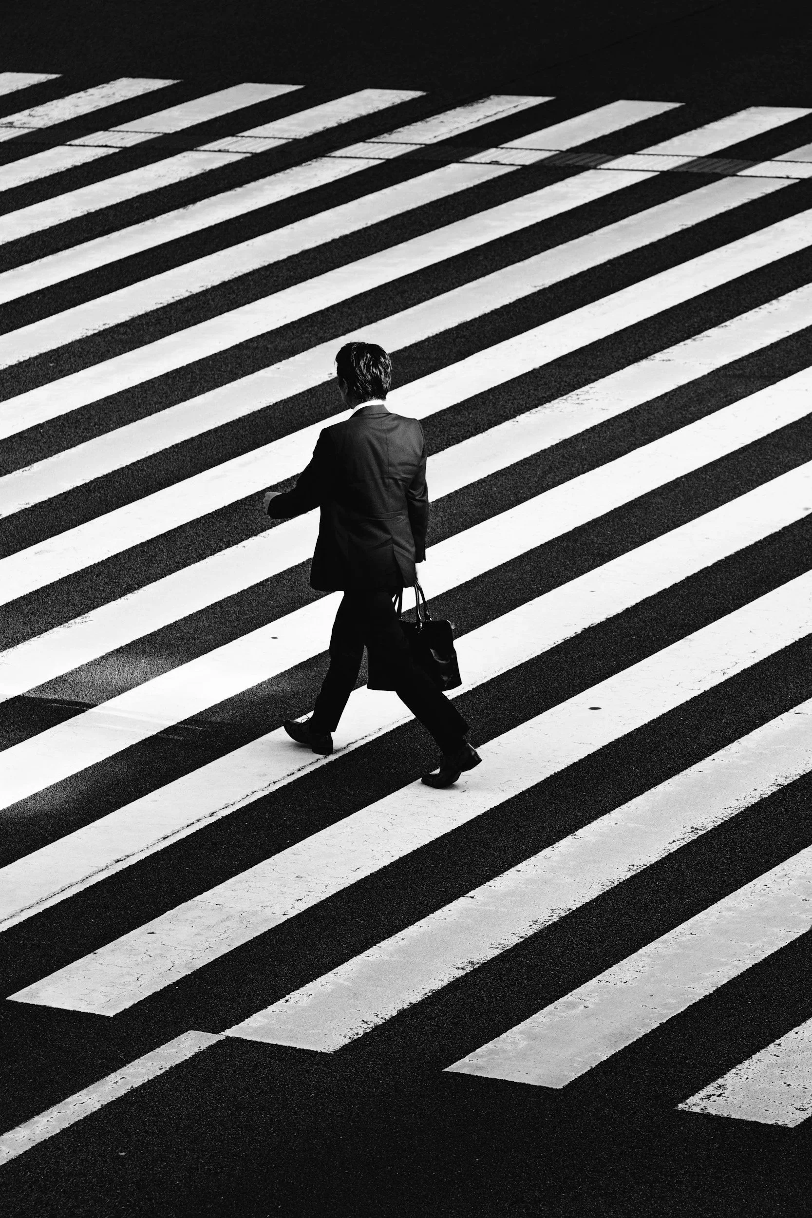 A man in a suit walking across a black and white striped crosswalk, carrying a briefcase.