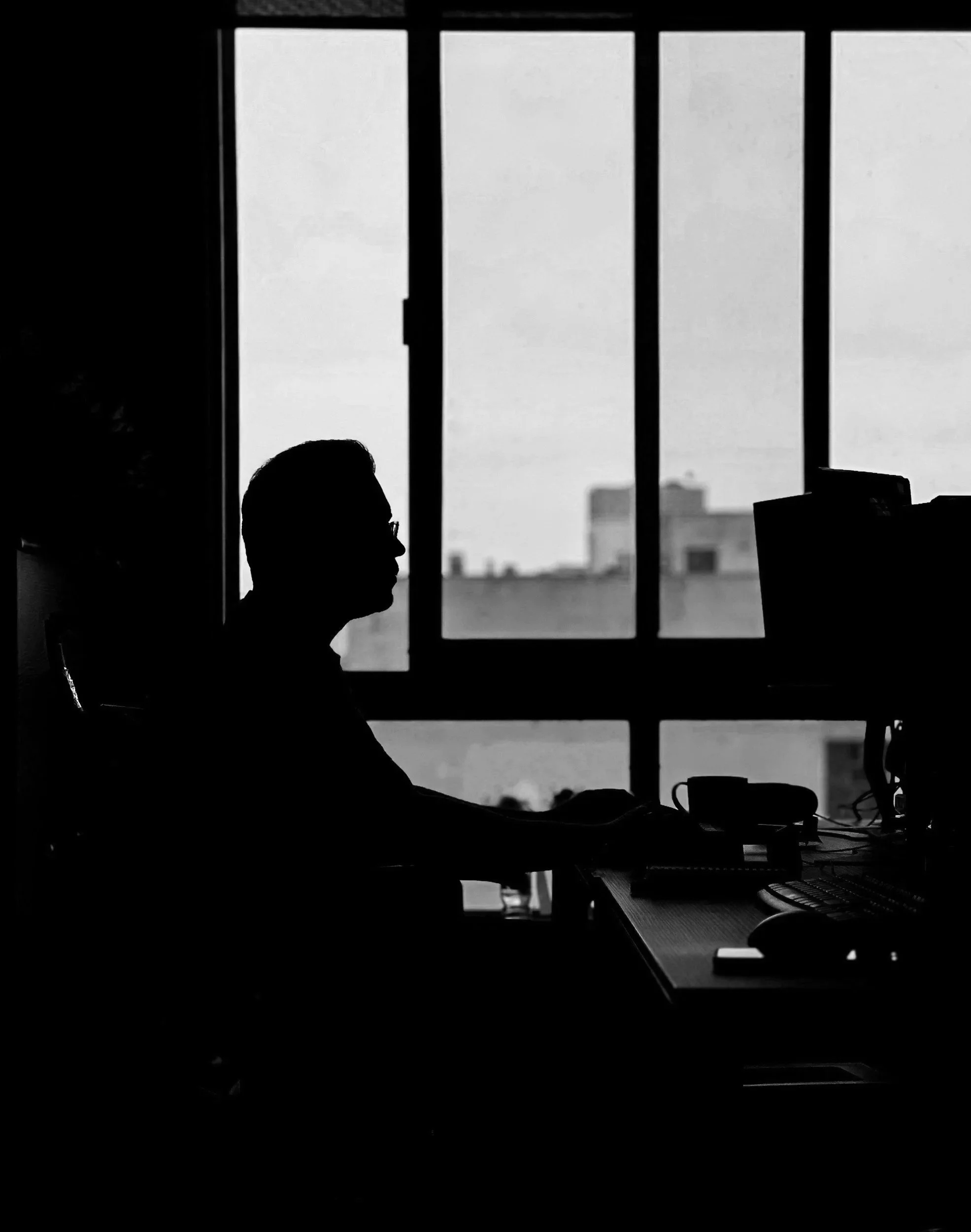 Silhouette of a person working at a desk in front of a large window with a city skyline outside.