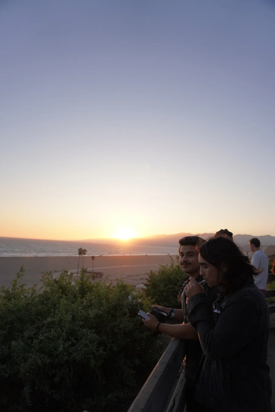 Matt blocha and Flight By Nothing's drummer Sam Morales Group of people watching a sunset over the ocean from a viewpoint, with some people looking at their phones and others enjoying the scenery.