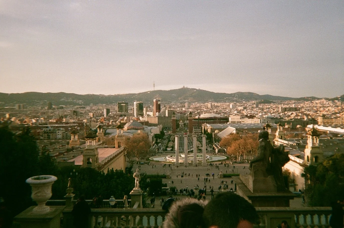 View of San Francisco skyline from a hill, with buildings, trees, and a viewing platform in the foreground, and green hills in the background.