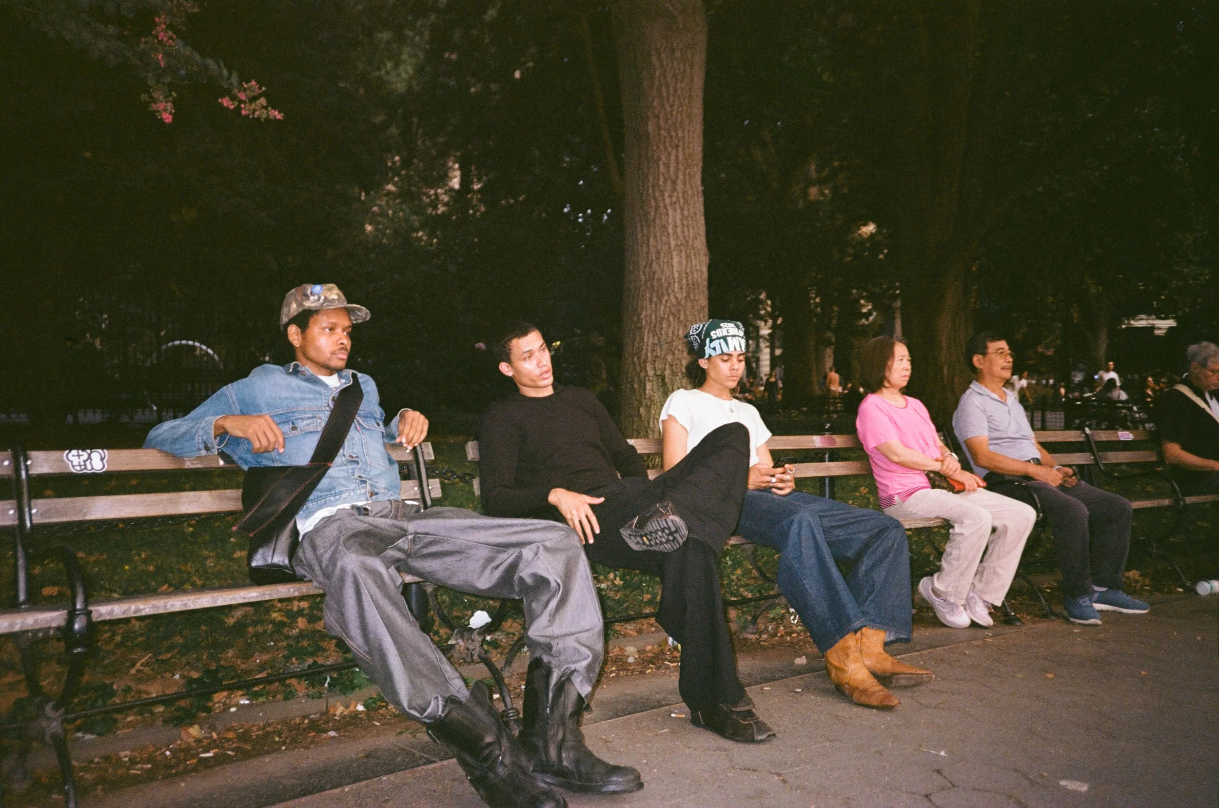 Five people sitting on park benches at night, with trees in the background.